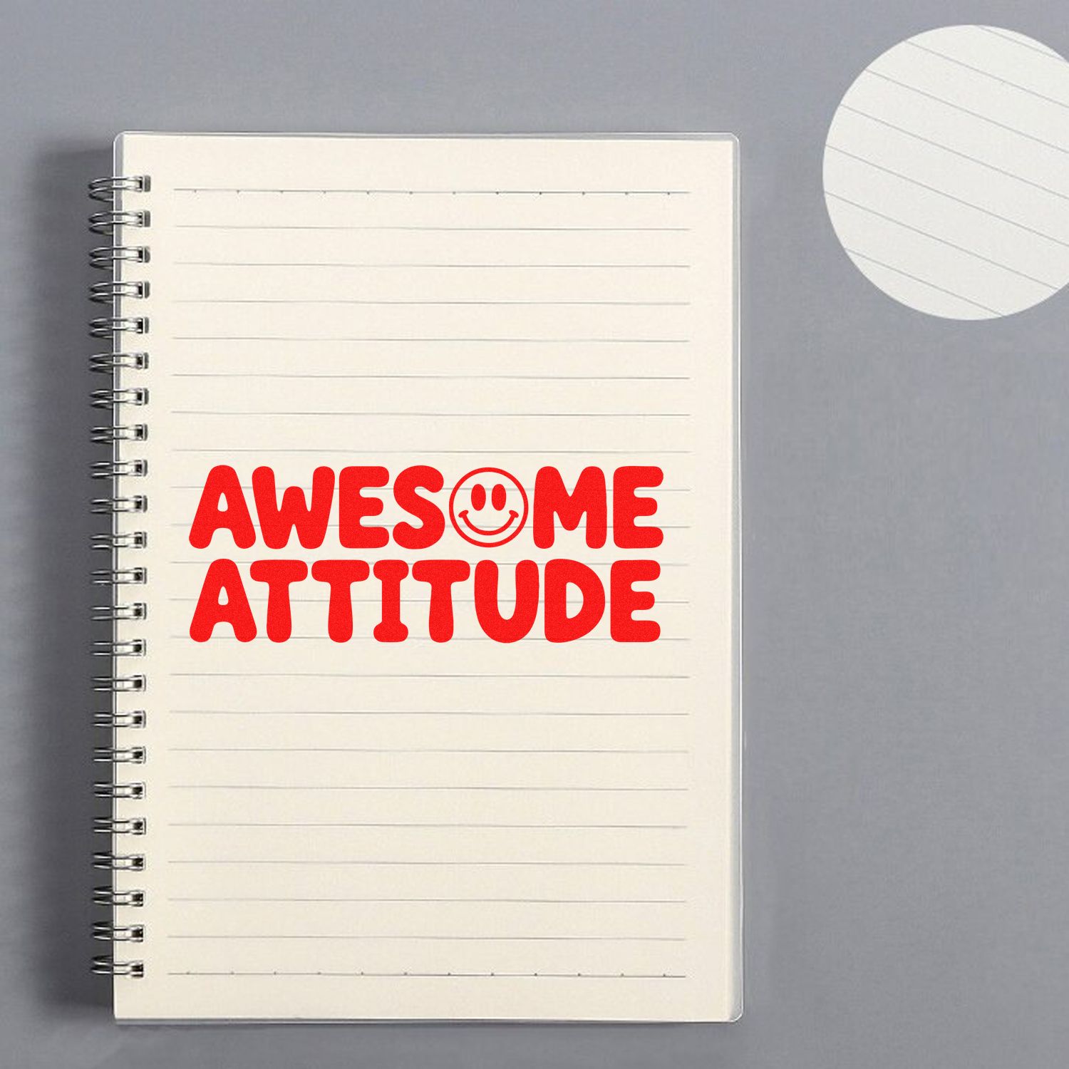 Red Awesome Attitude stamp on a cream spiral notebook with smiley seal, beside a white round seal pad on gray.