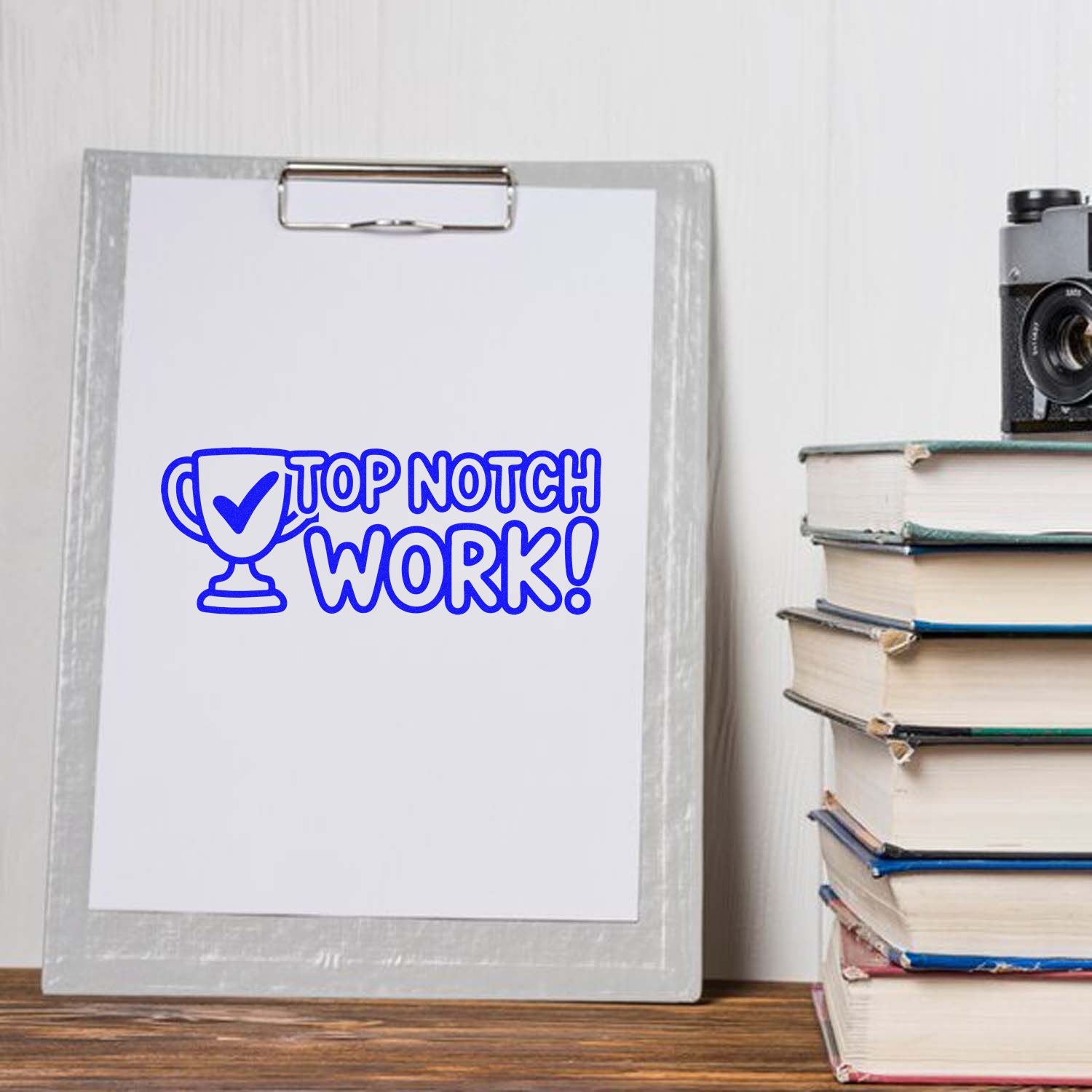 Blue custom stamp and seal design reading Top Notch Work! with trophy icon on a clipboard beside stacked books.