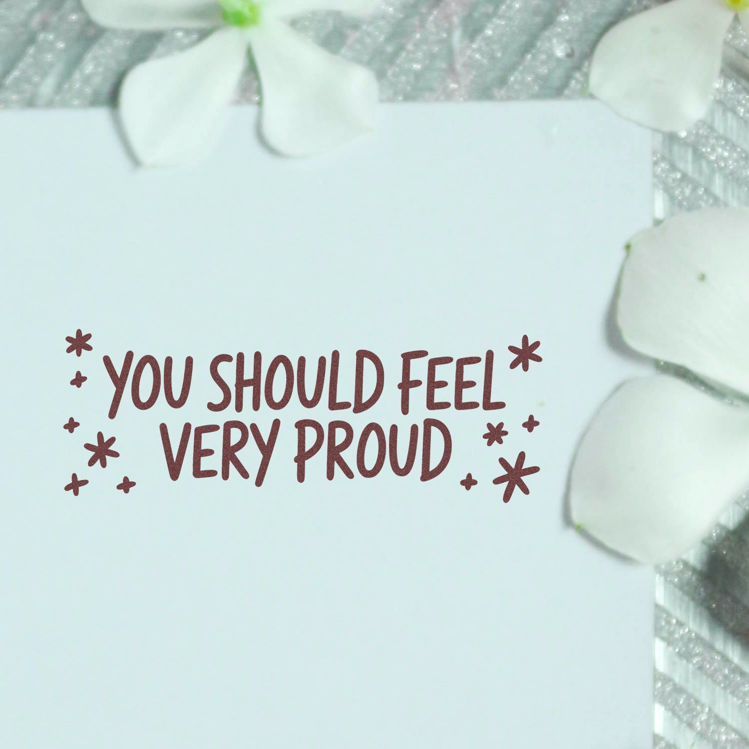 Maroon motivational rubber stamp on white seal sheet, reading You Should Feel Very Proud, with white petal accents.