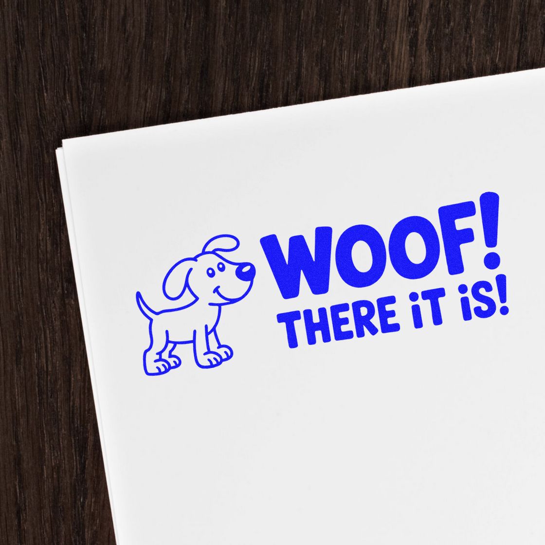 Blue dog stamp and seal reading WOOF! THERE IT IS! on white paper against dark wood.
