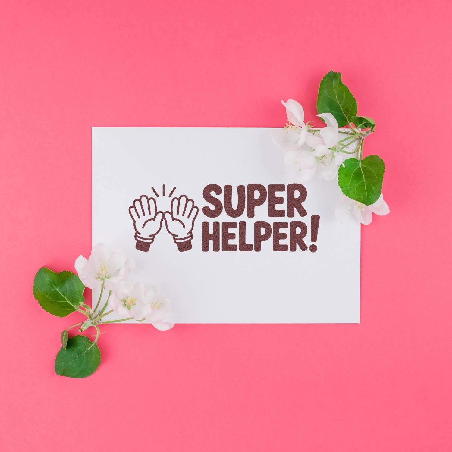 Brown Super Helper stamp seal with clapping hands on a white card, framed by white blossoms and green leaves on a pink background.