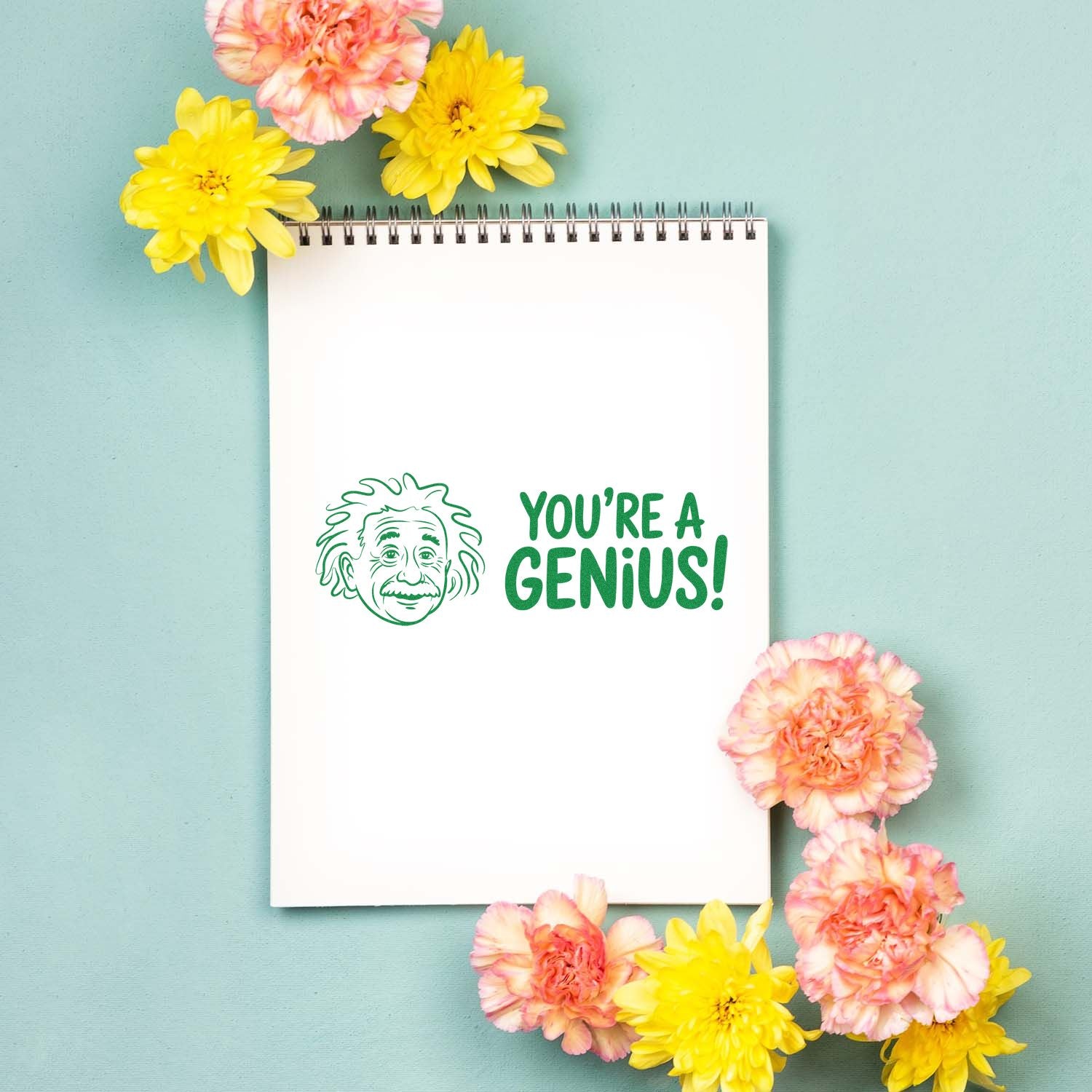 Green 'You're a Genius!' stamp and seal with Einstein face on white notepad, framed by yellow and peach flowers on mint background.