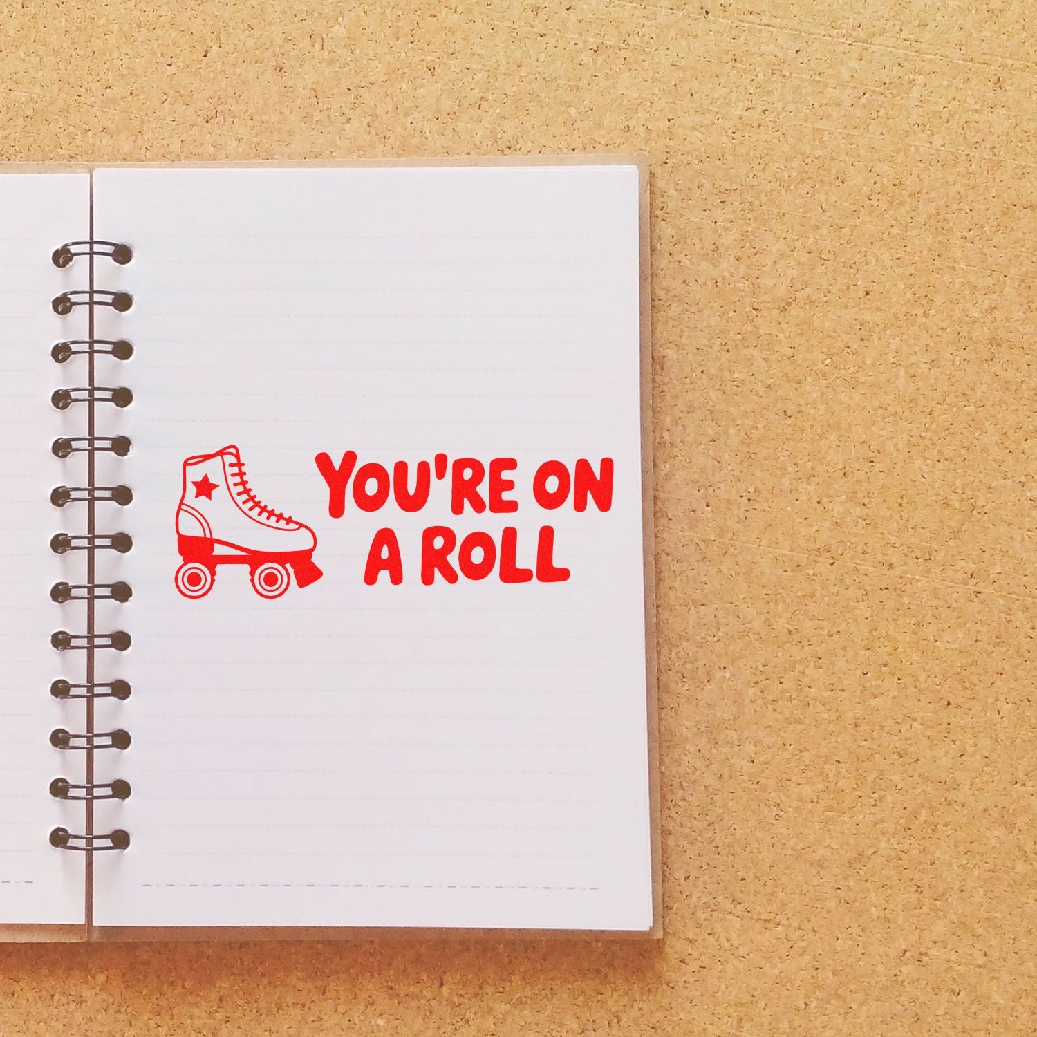 Red roller skate stamp and seal with YOURE ON A ROLL on a white spiral notebook page.