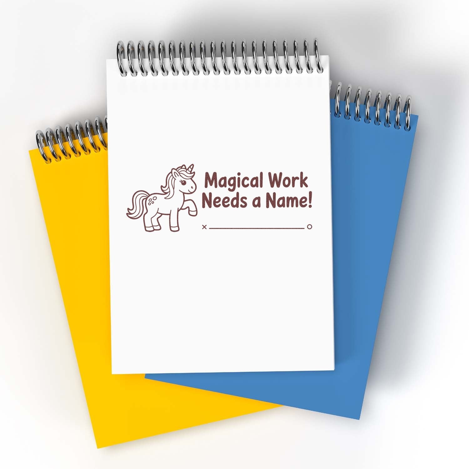 Unicorn-themed stamp seal on white spiral notebook, with yellow and blue pads and Magical Work Needs a Name! text.