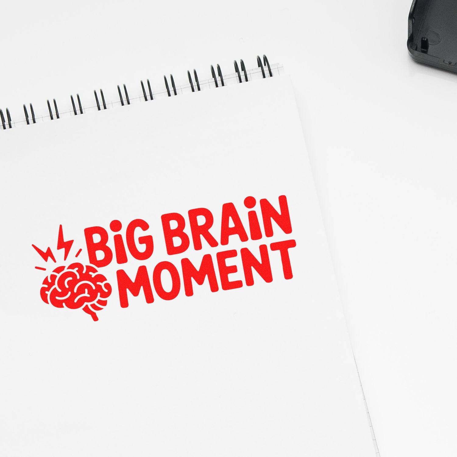 Red BIG BRAIN MOMENT stamp on a white spiral notebook with brain icon; black stamp seal case in corner.