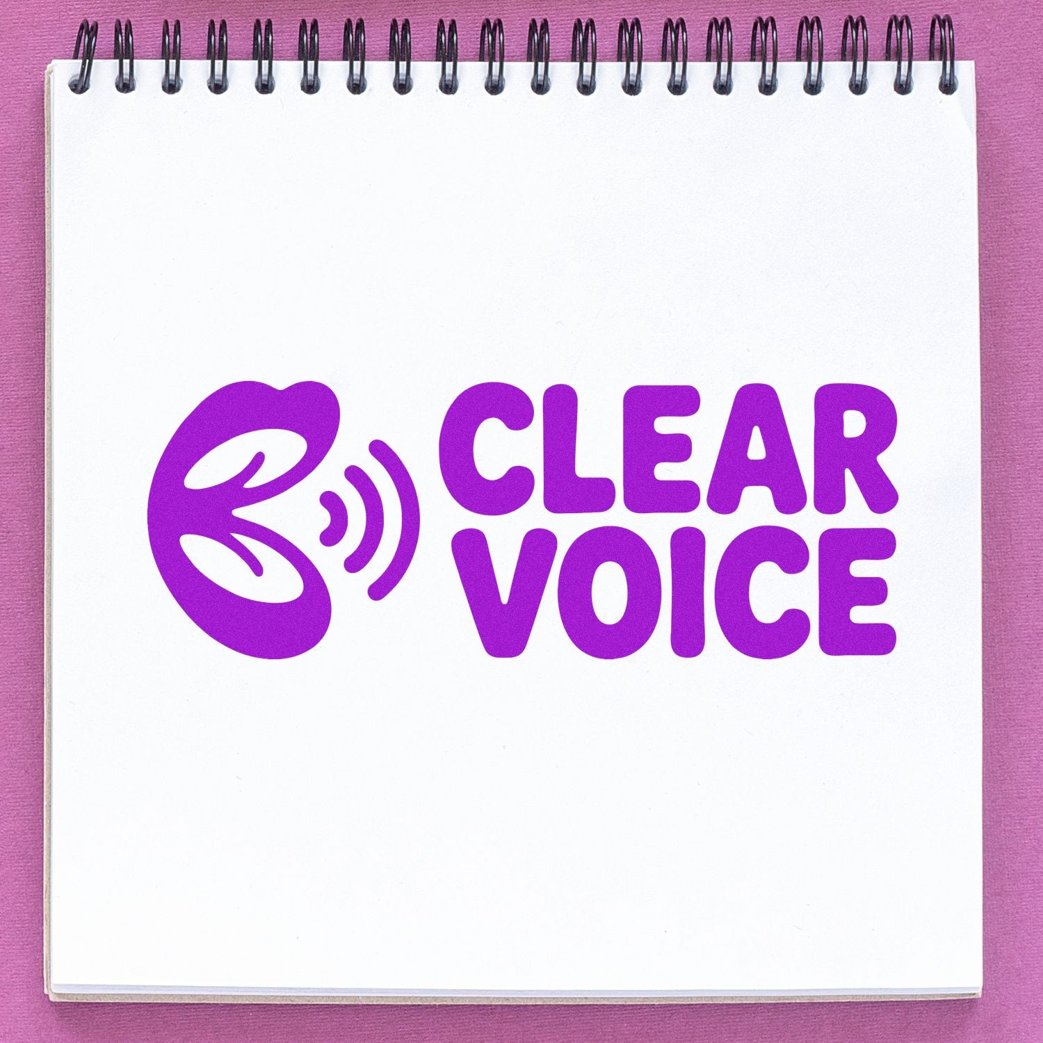 Purple CLEAR VOICE stamp and seal logo on a white spiral notepad, with a pink background.