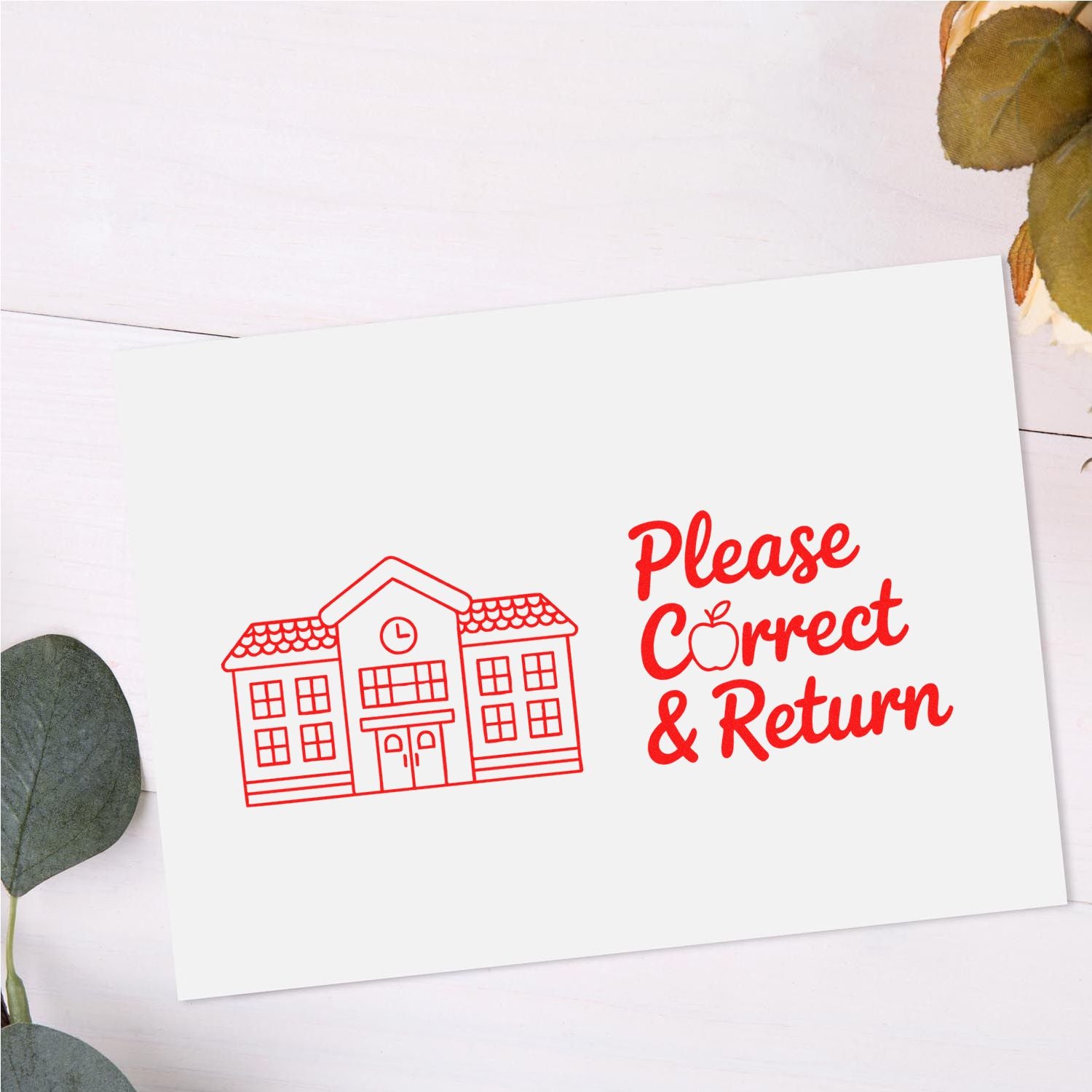 Red Please Correct & Return rubber stamp with schoolhouse seal on white card, accented by dried leaves