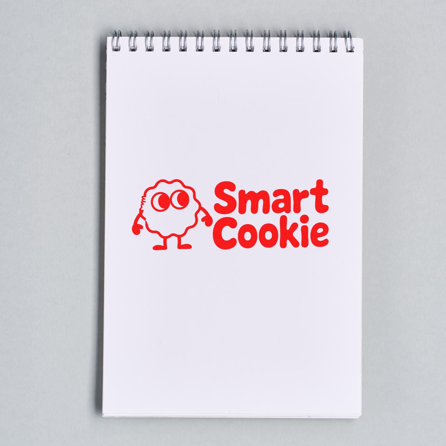 Red Smart Cookie rubber stamp and seal on a white spiral notepad, with a cartoon cookie mascot in bold red.