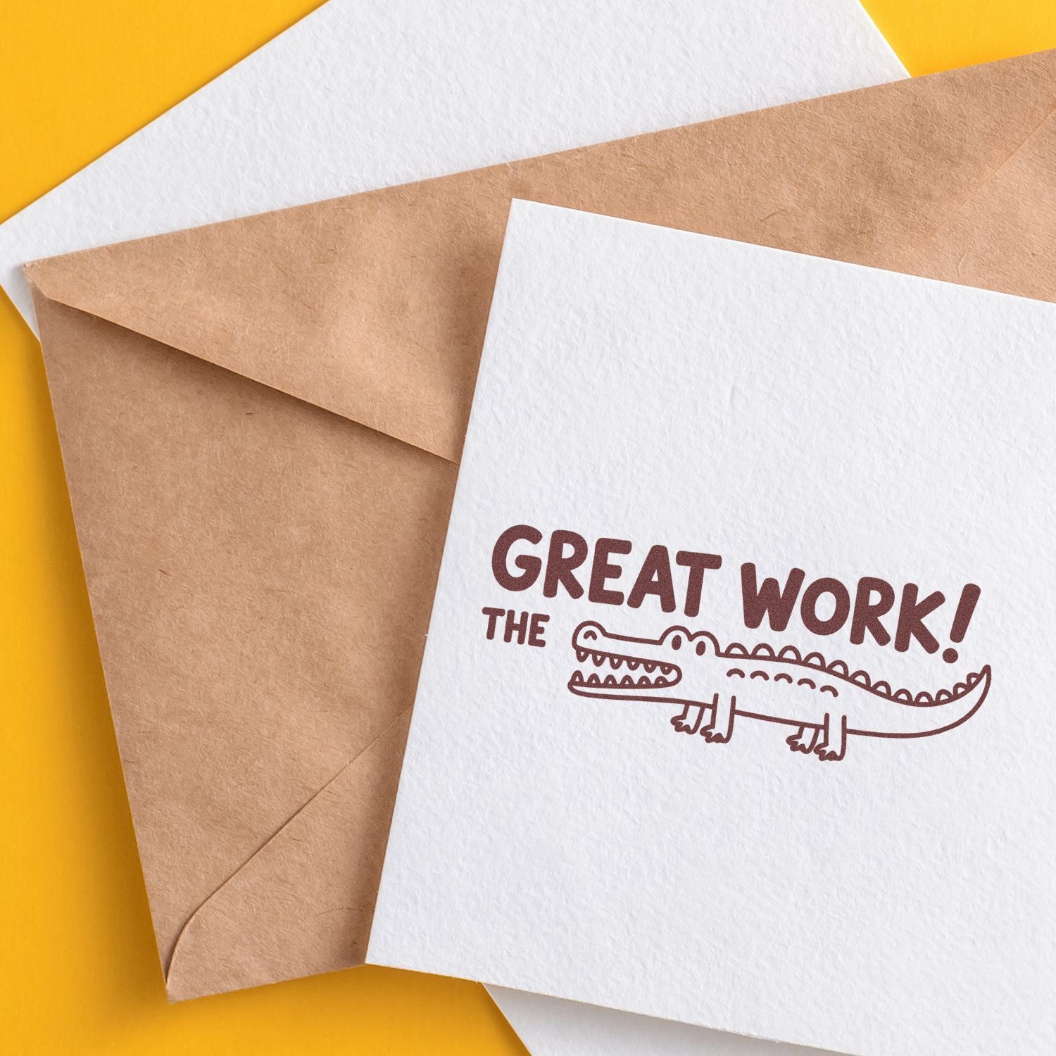 White card with brown Great Work! crocodile stamp, beside kraft and white envelopes on a yellow background.