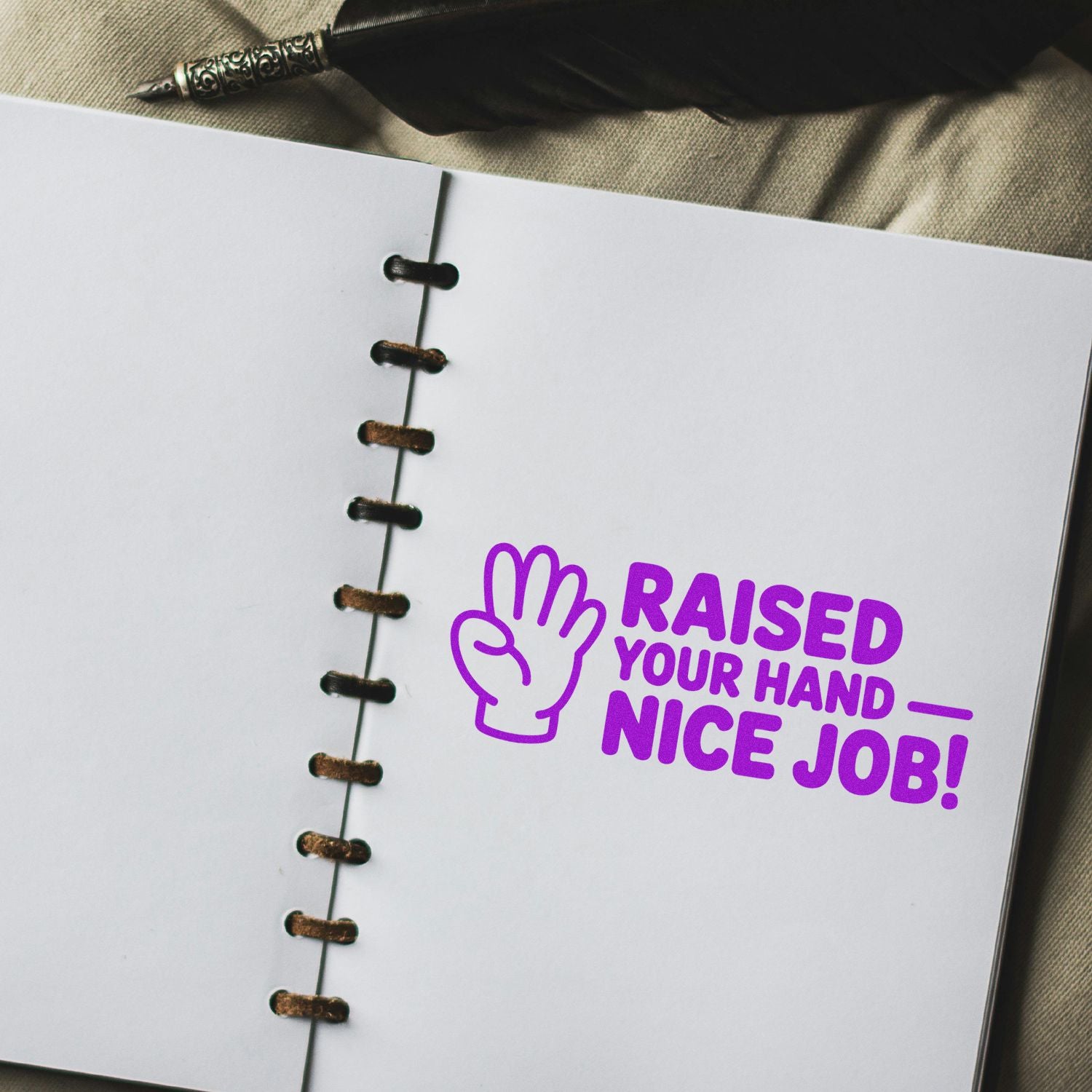 Purple stamp seal with hand icon and bold RAISED YOUR HAND NICE JOB! on a white notebook page, beige background.