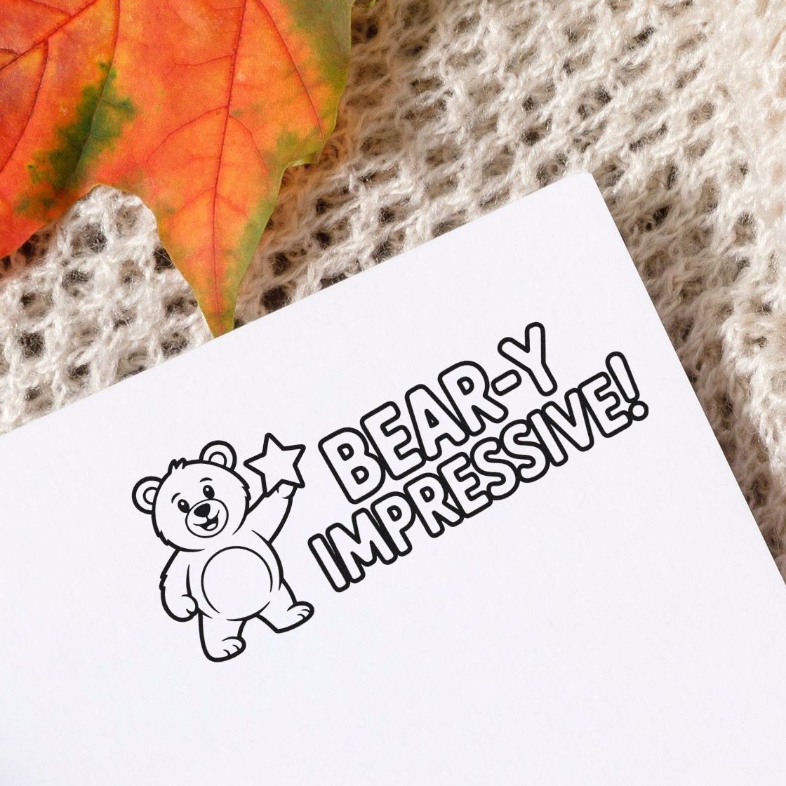 Black bear stamp and seal with star and BEARY IMPRESSIVE! on white paper, beside an orange leaf.