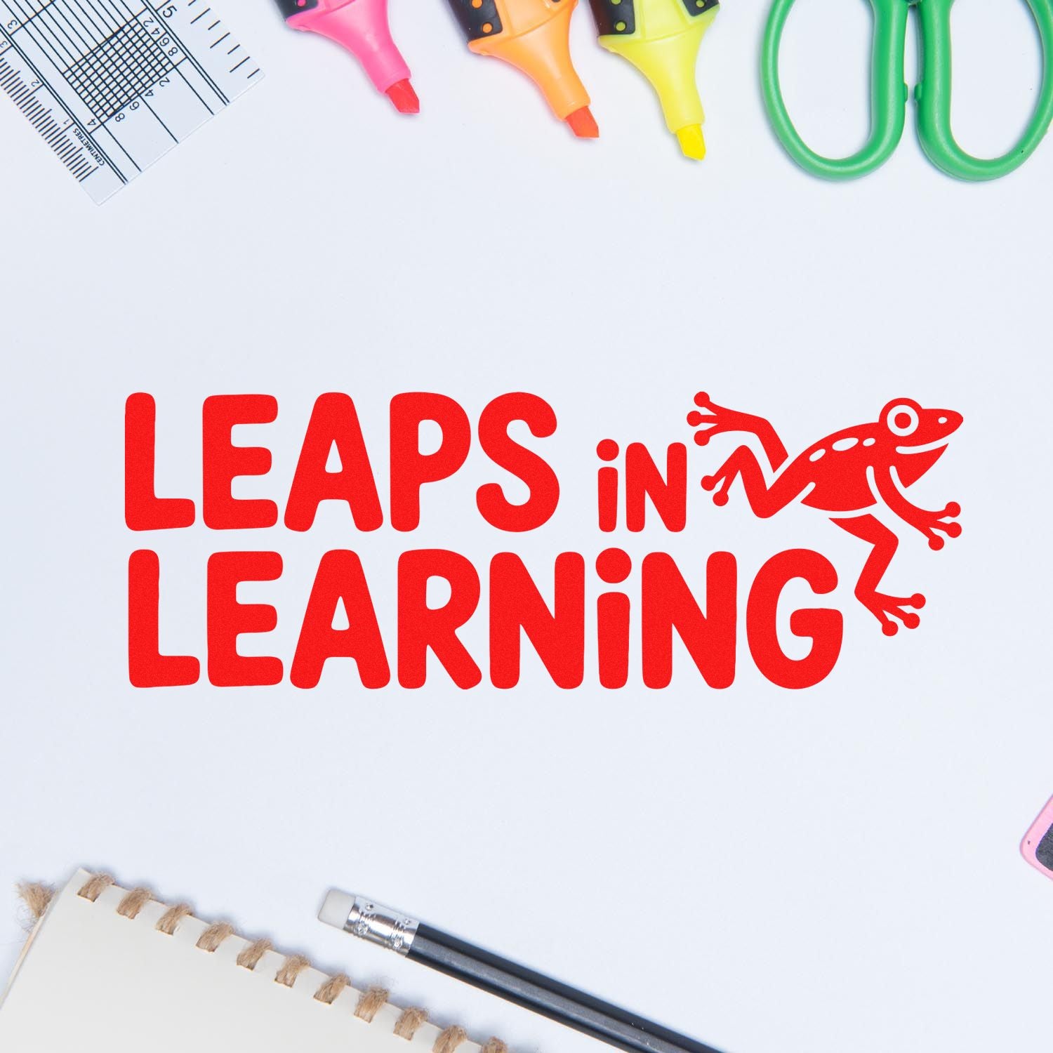 Red LEAPS IN LEARNING rubber stamp seal with frog, surrounded by colorful markers, ruler, scissors, pencil, and notebook on white
