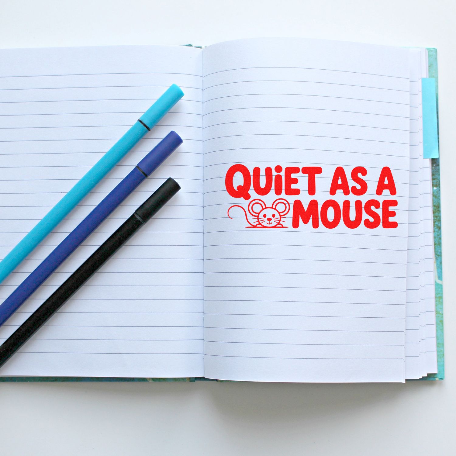Notebook with three pens and a red stamp seal reading Quiet as a Mouse with mouse icon.