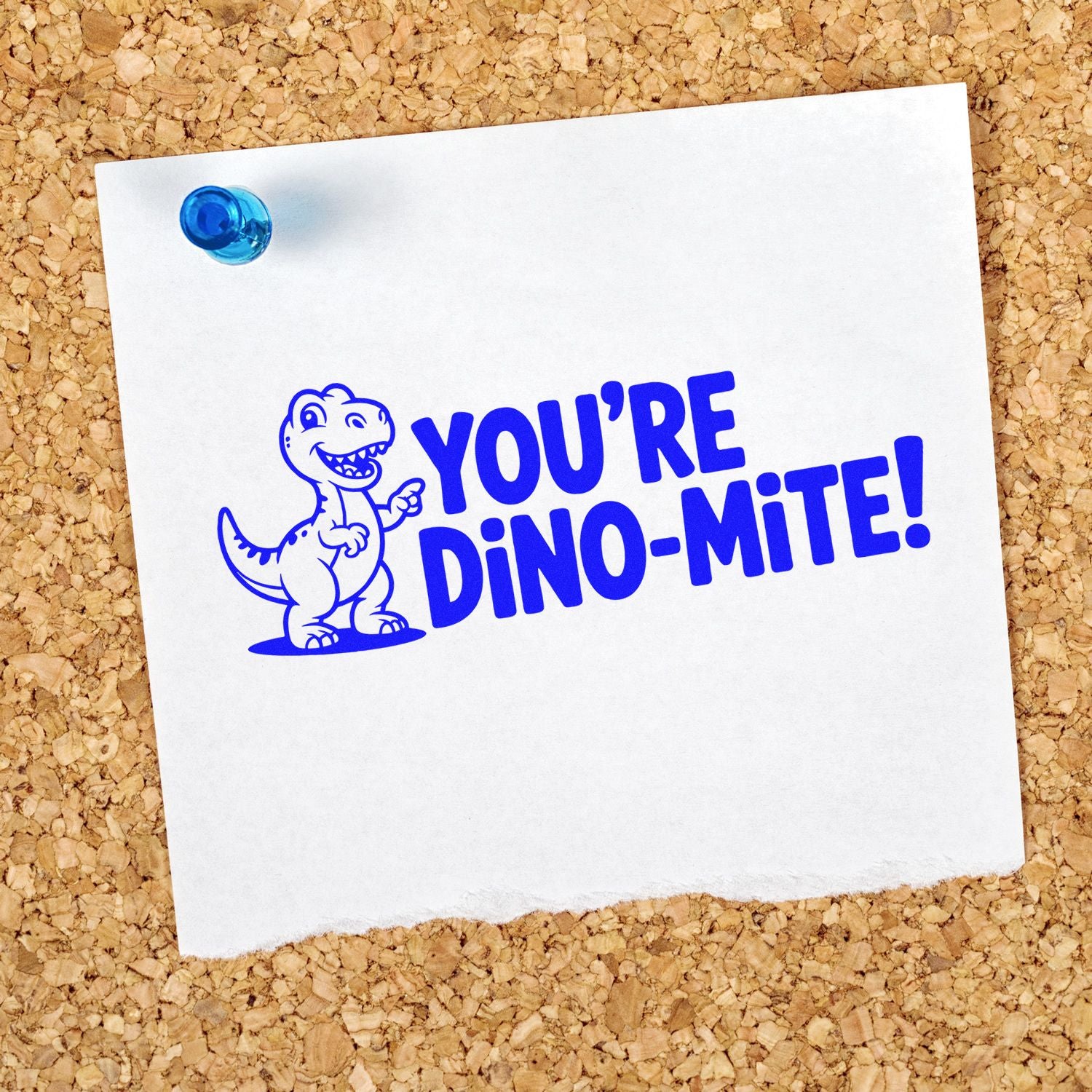 Blue dinosaur stamp and seal reading "YOU'RE DINO-MITE!" on white paper pinned to corkboard with a blue pushpin.