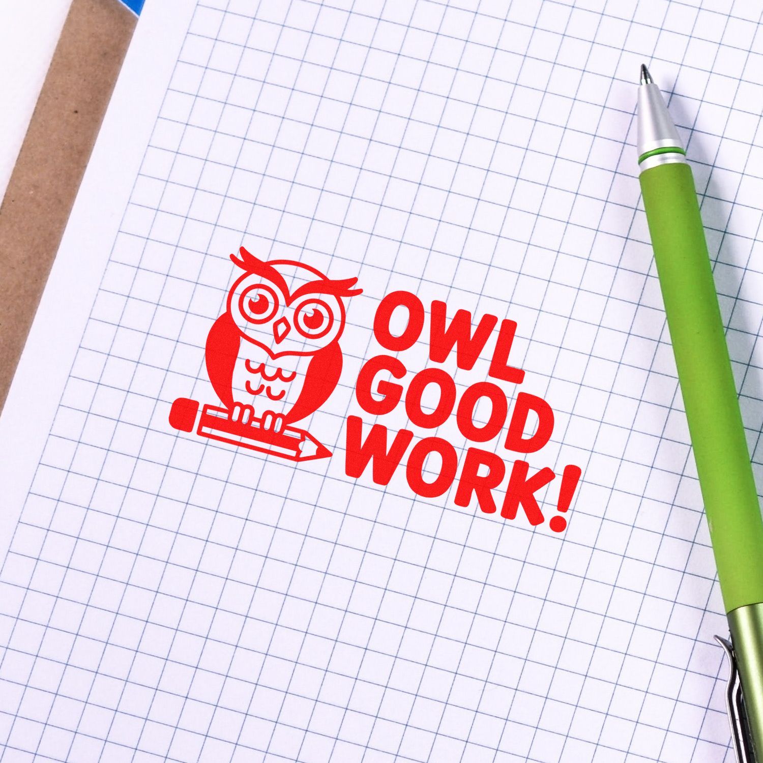 Red owl Good Work! rubber stamp seal on graph paper beside a green pen