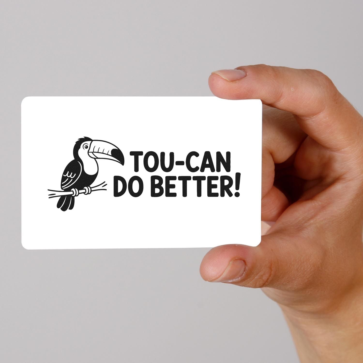 Hand holding white stamp seal card with black toucan graphic and TOU-CAN DO BETTER! text.