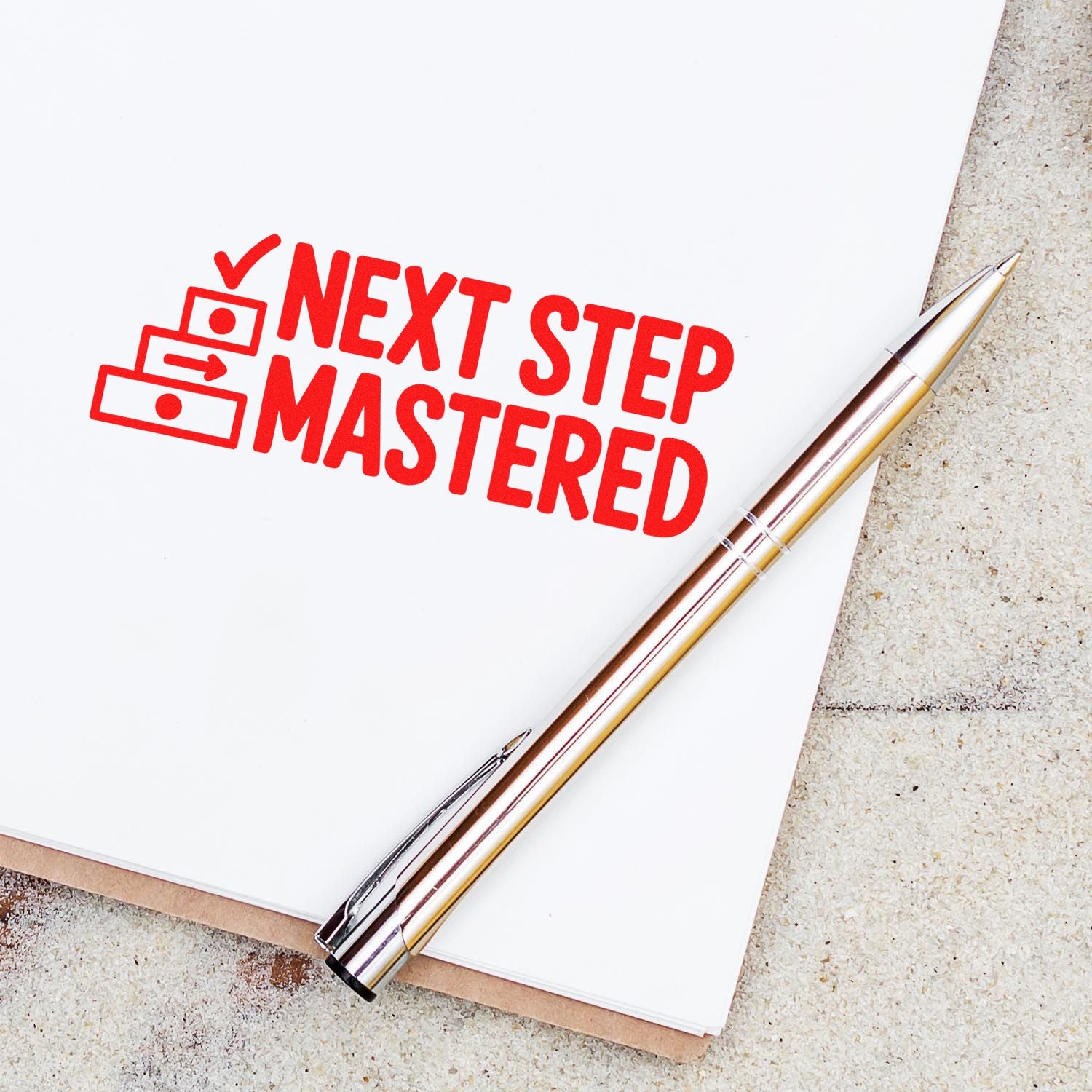 Red stamp and seal imprint reading "NEXT STEP MASTERED" on white paper, with checklist icon and silver-gold pen.