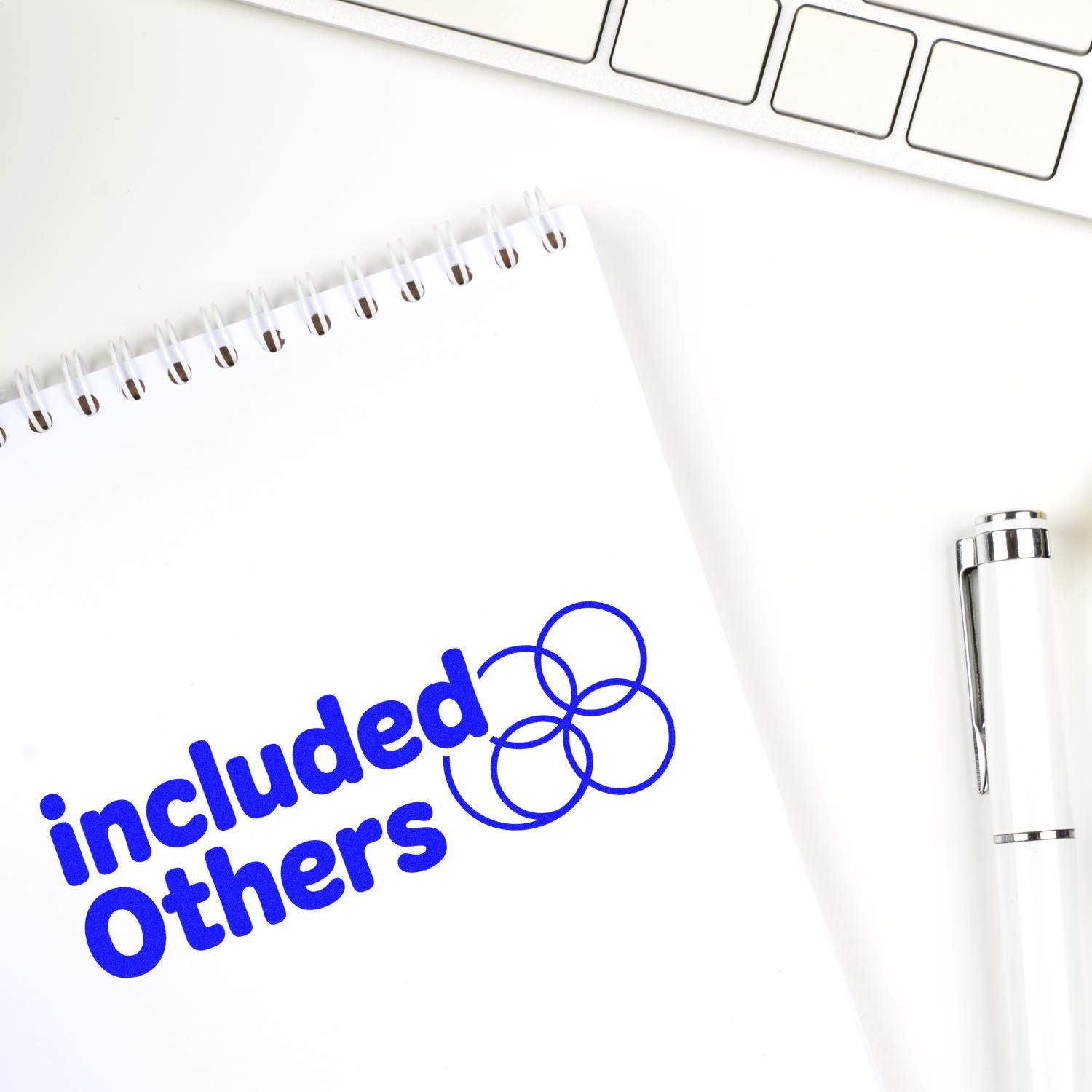 White notepad with blue included others stamp and seal circles, beside a silver pen and keyboard.