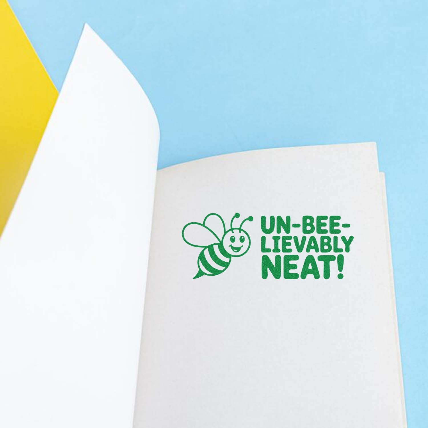 Green bee stamp and seal reading UN-BEE-LIEVABLY NEAT! on white paper, with light blue and yellow background.