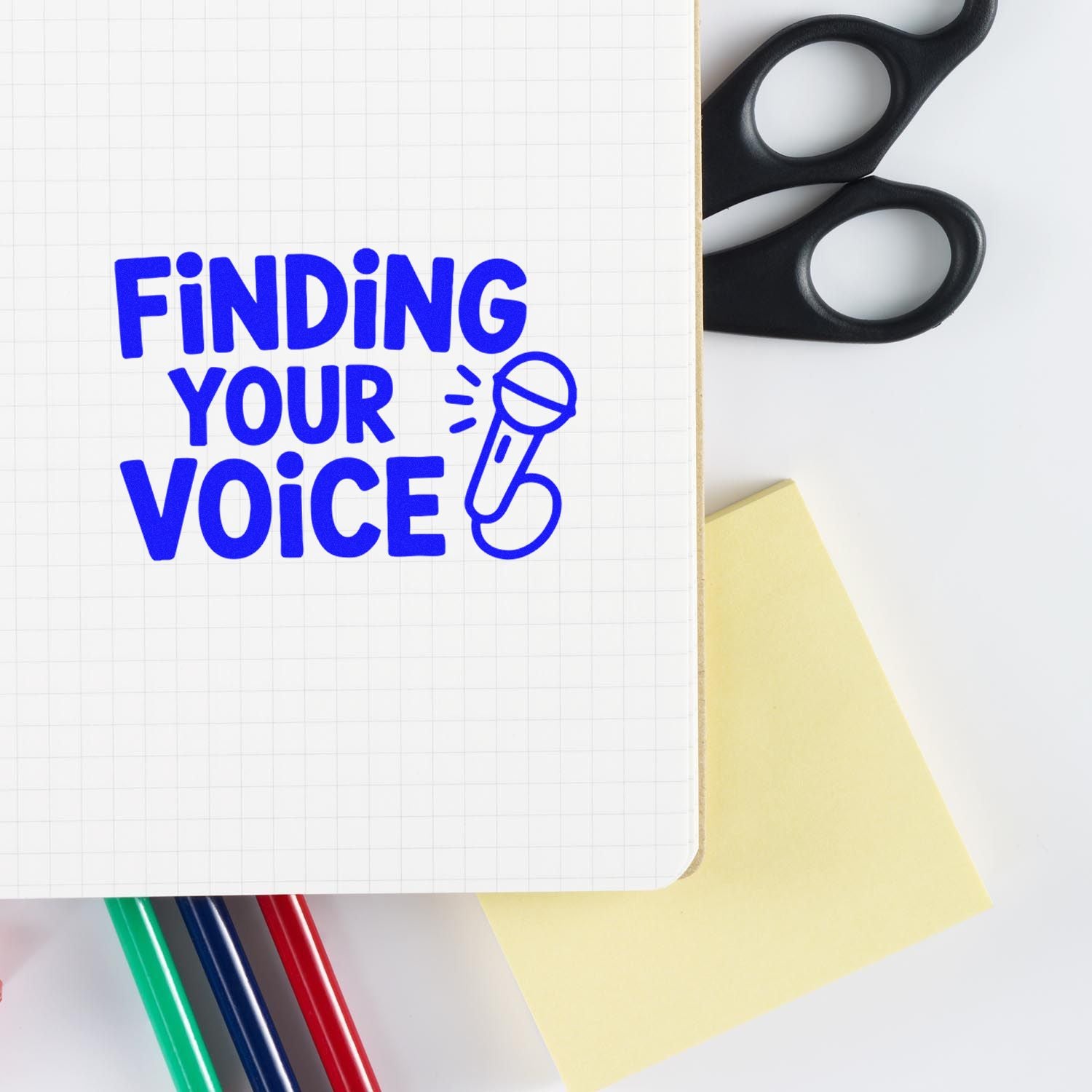 Blue Finding Your Voice stamp on grid paper, with black seal handles, yellow sticky note, and colored pens on white background