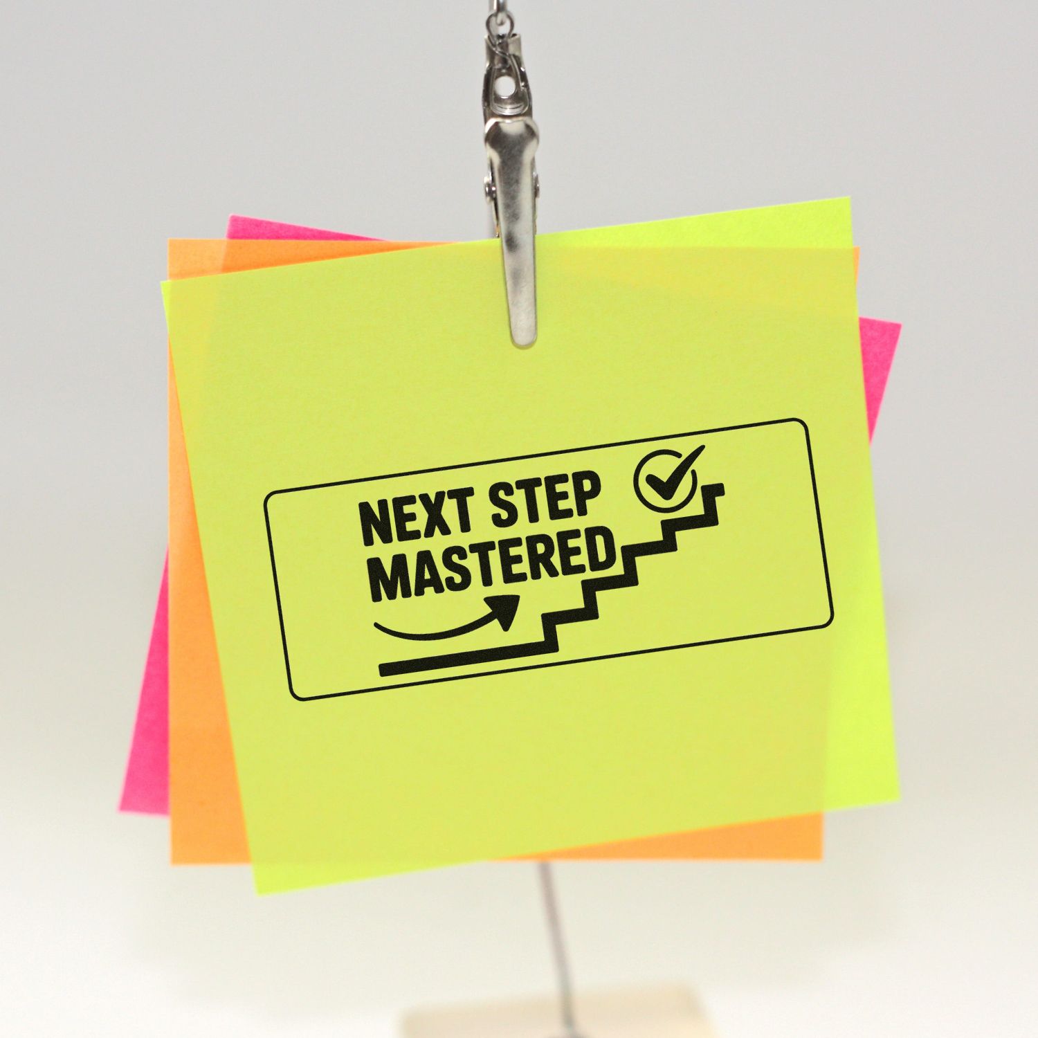 Neon green custom rubber stamp seal reading Next Step Mastered, clipped over pink and orange notes with checkmark and stairs icon.