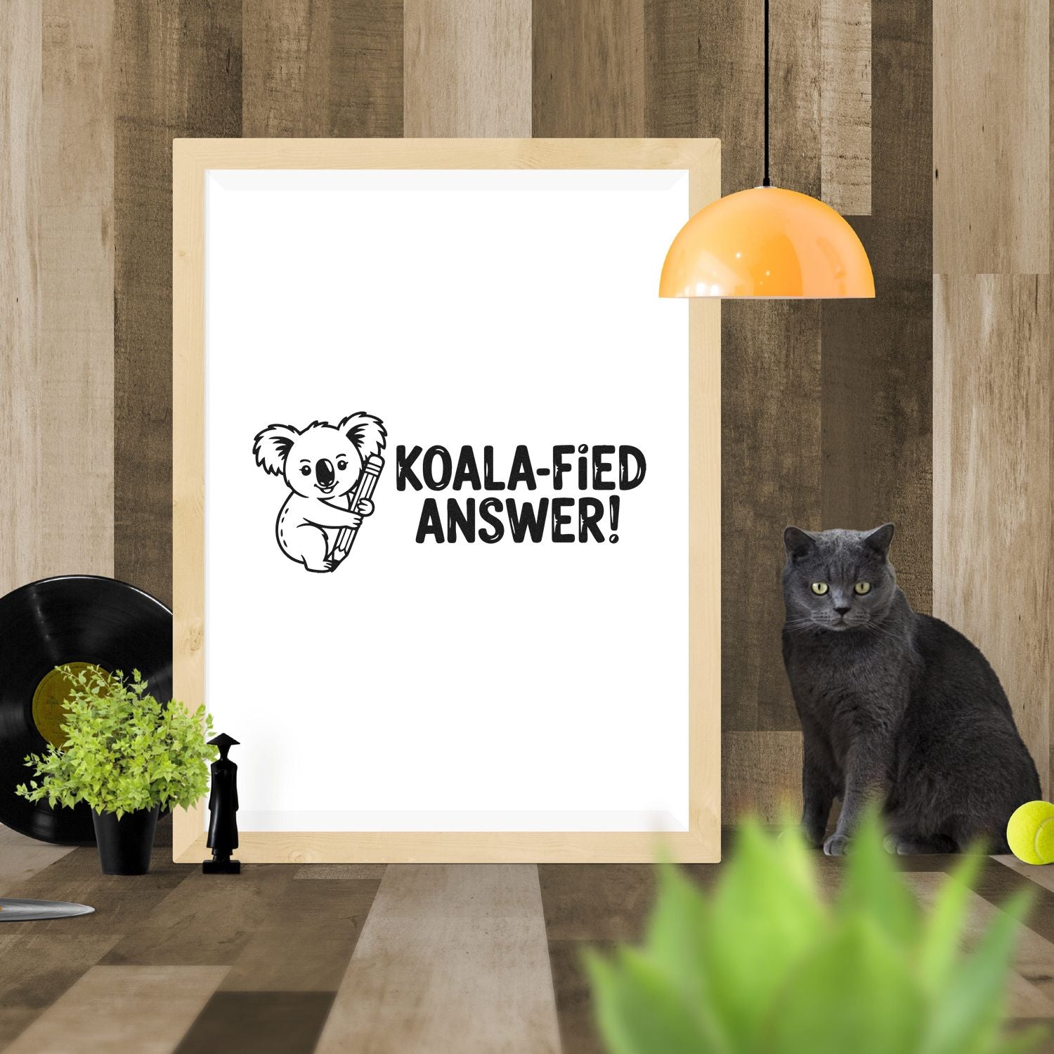 Black koala stamp design with Koala-fied Answer! on a white framed seal mockup against warm wood tones.