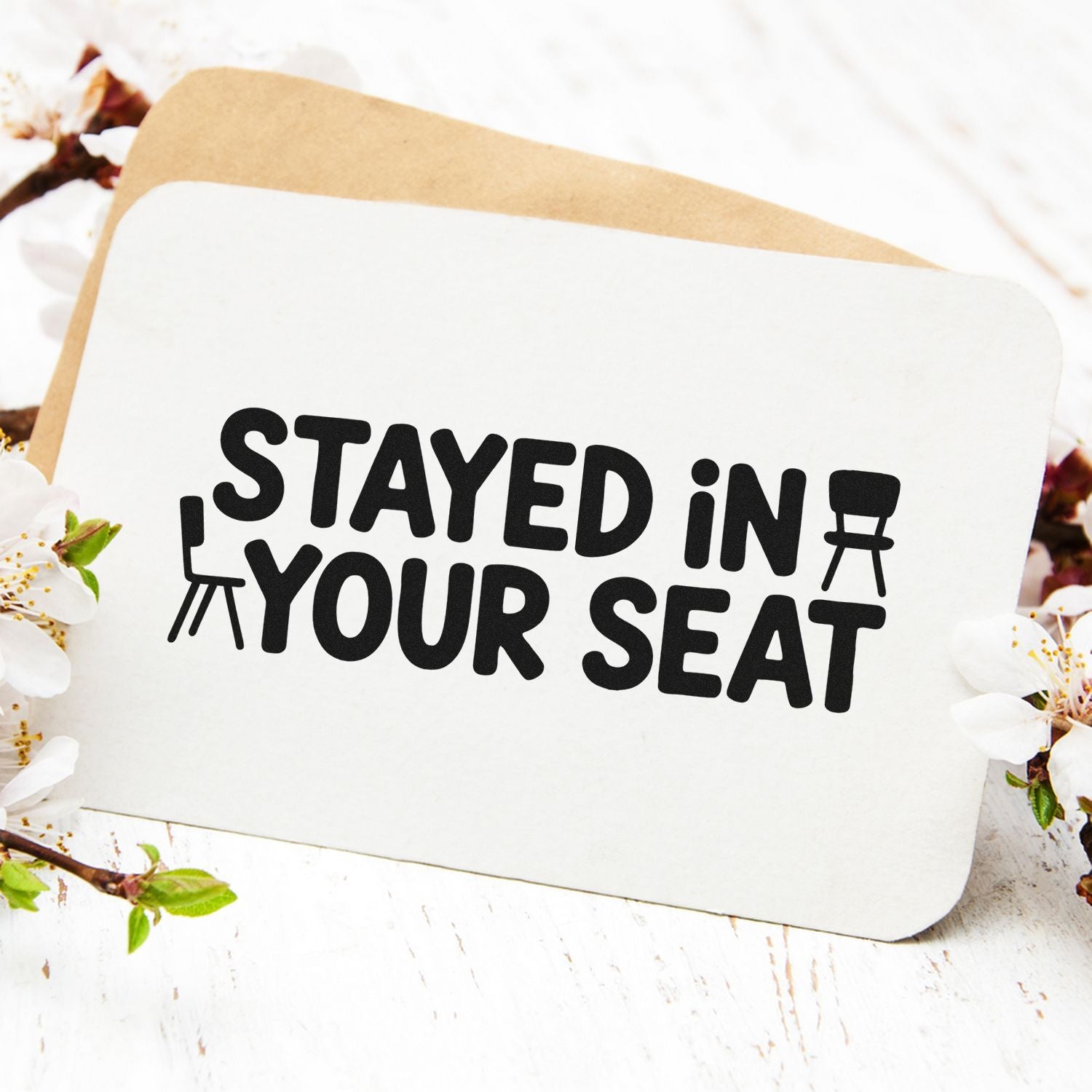 Custom stamp and seal on white card with black STAYED IN YOUR SEAT text and chair icons, on tan backing.
