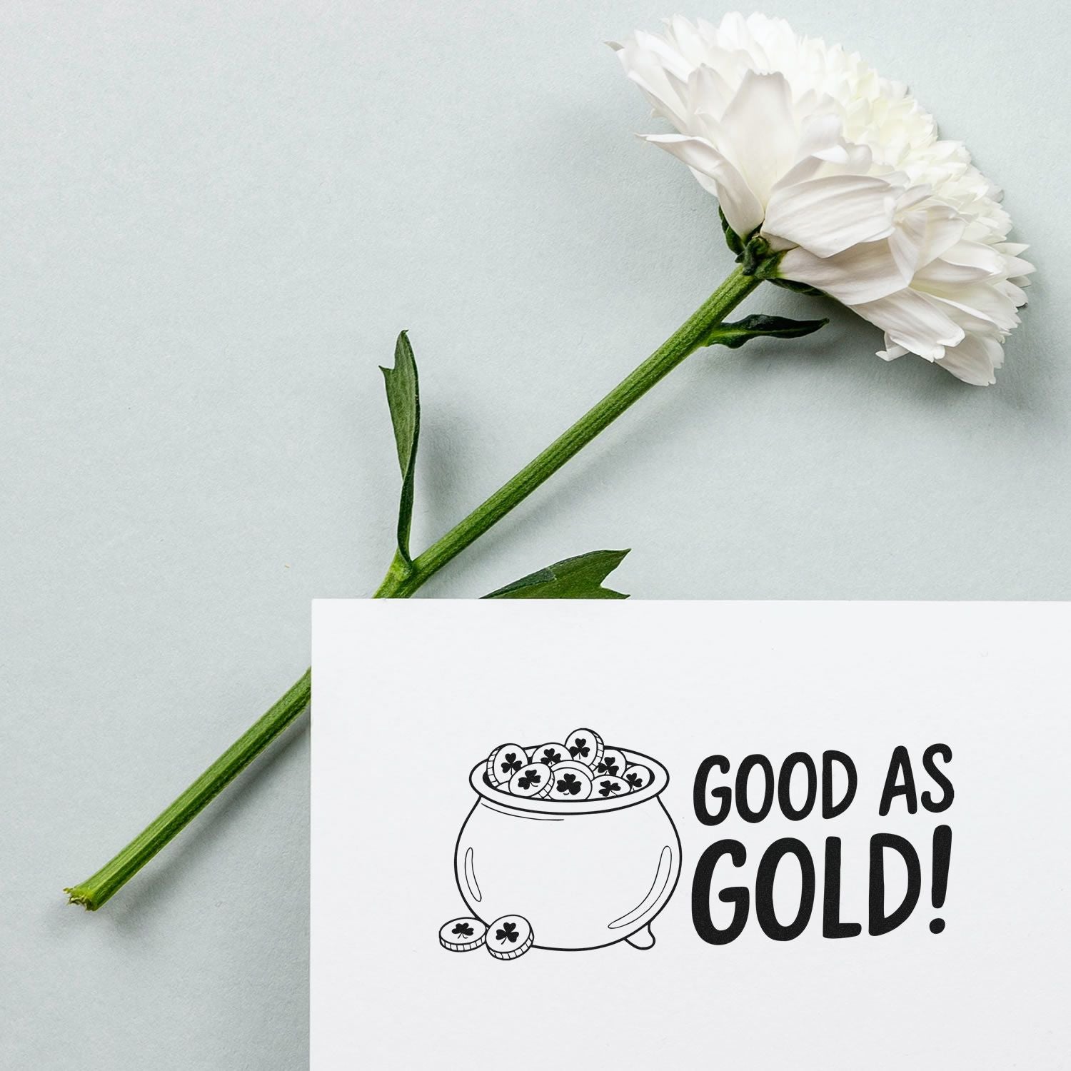 Stamp and seal design with white flower, reading GOOD AS GOLD!, featuring a black pot of gold and clover coins.