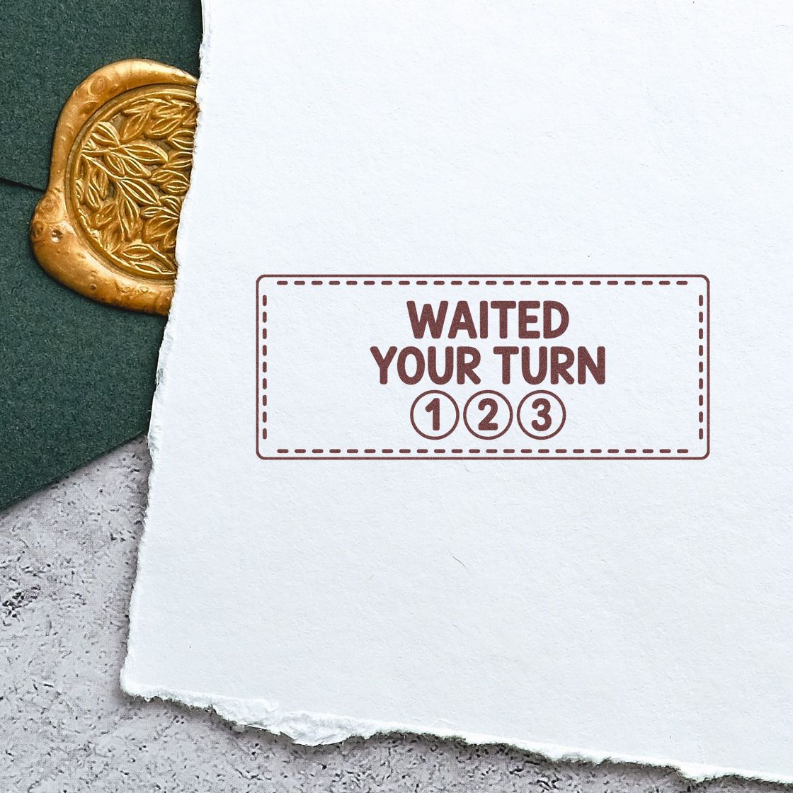 Maroon rubber stamp reading WAITED YOUR TURN 1 2 3 on white paper, beside a gold embossed seal and dark green paper.