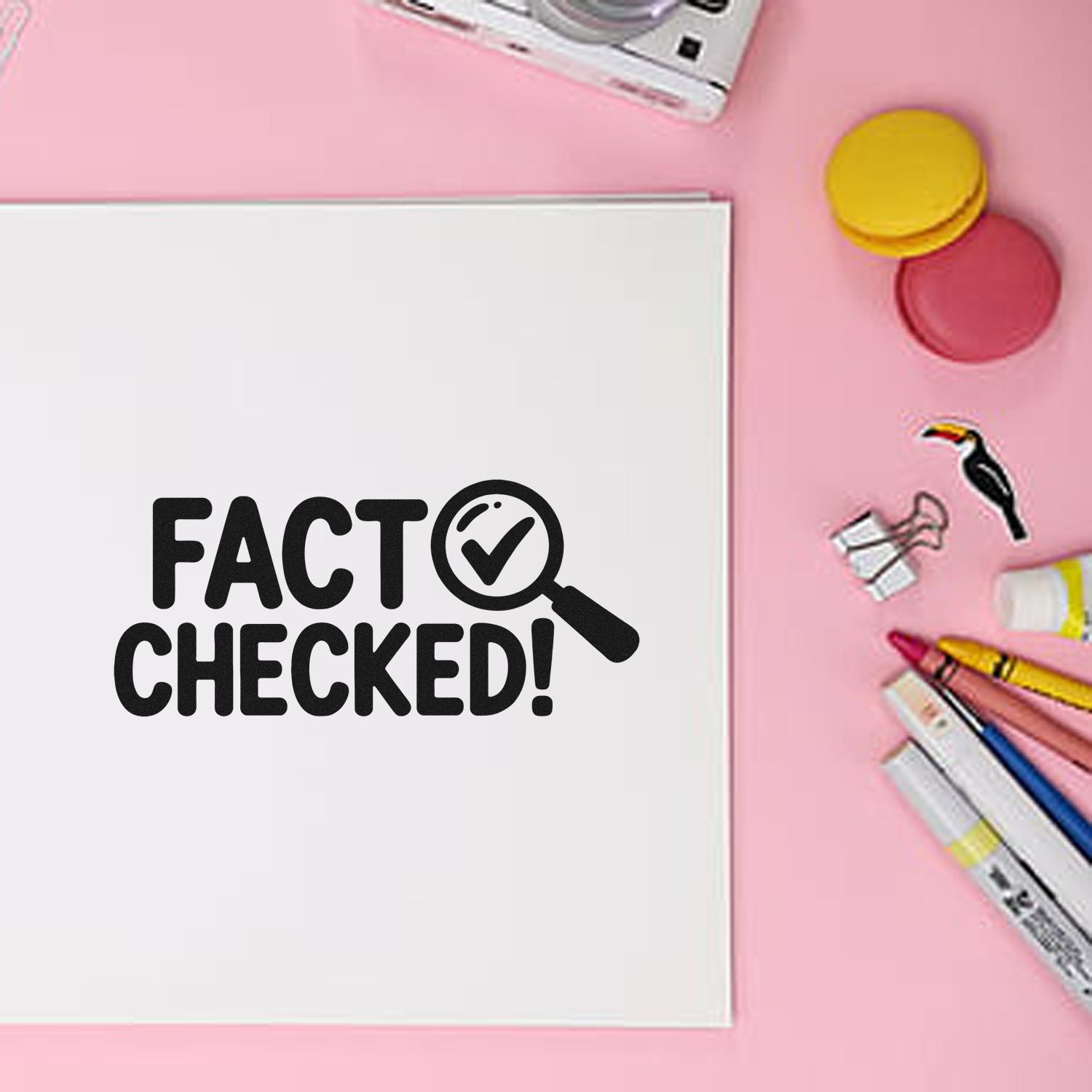 Black Fact Checked! stamp on white paper, with yellow and pink seal wax, pens and clips on a pink background.