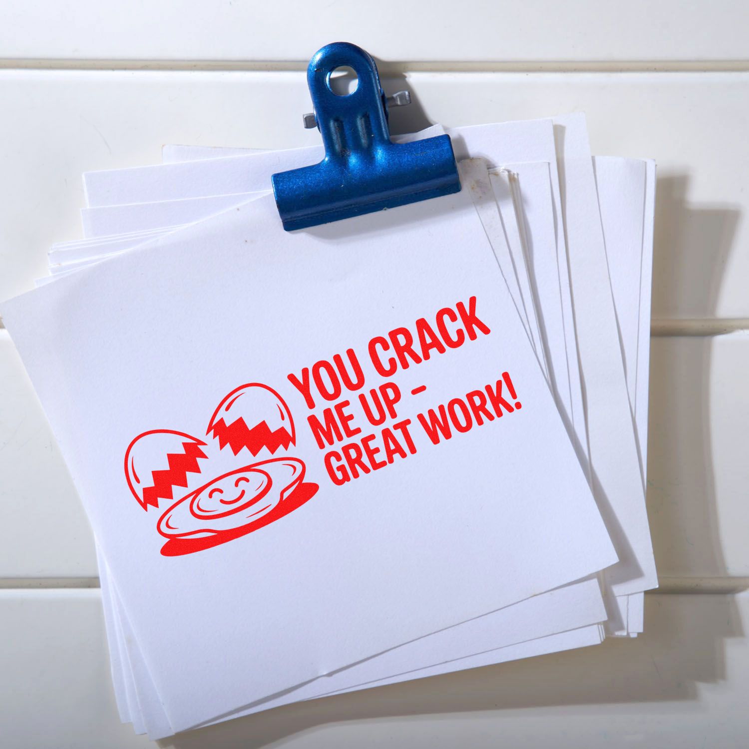 Blue binder clip holding white stamp and seal cards with red cracked-smiley seal and You crack me upgreat work! text.
