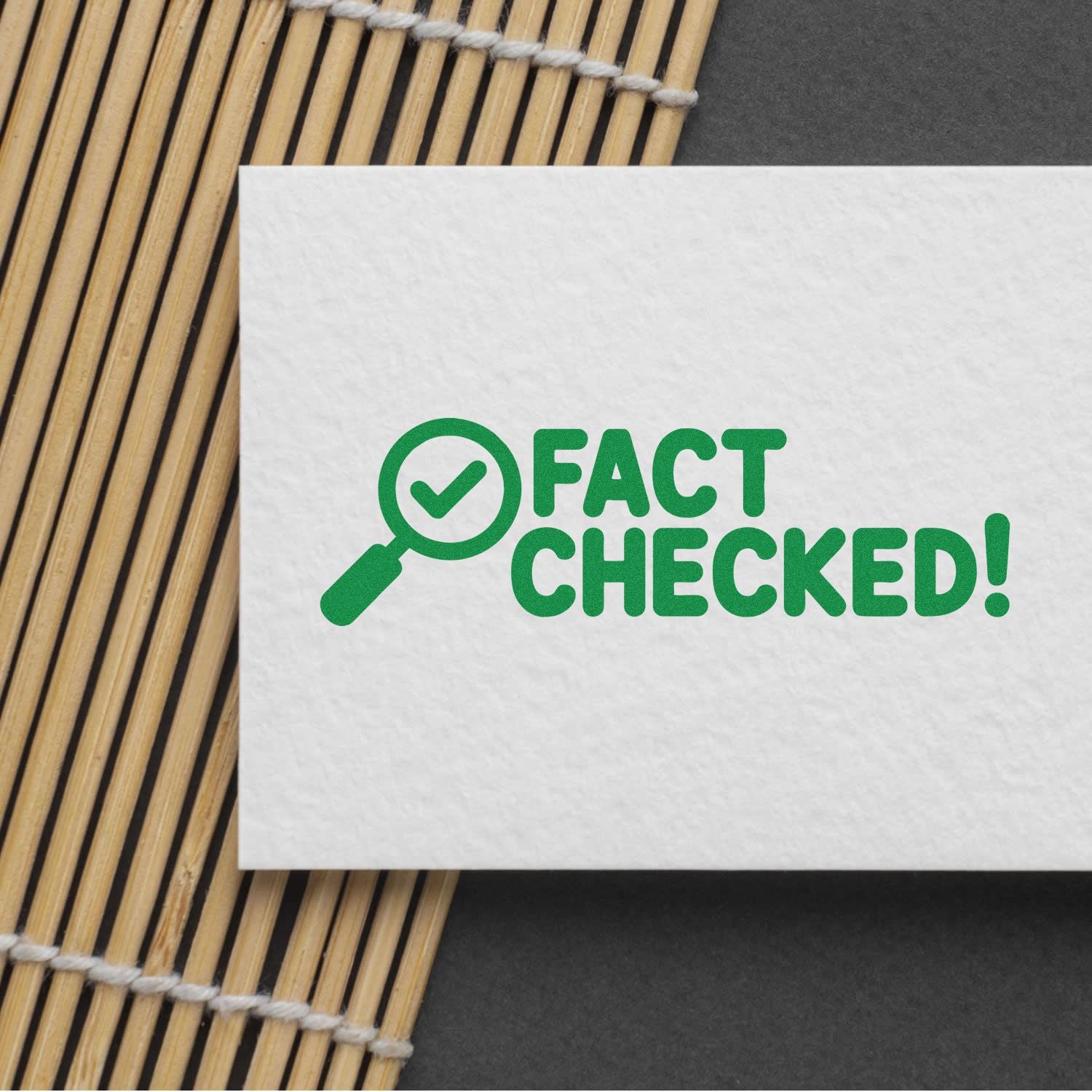 Green FACT CHECKED! stamp and seal on white card with magnifying glass checkmark over bamboo mat backdrop