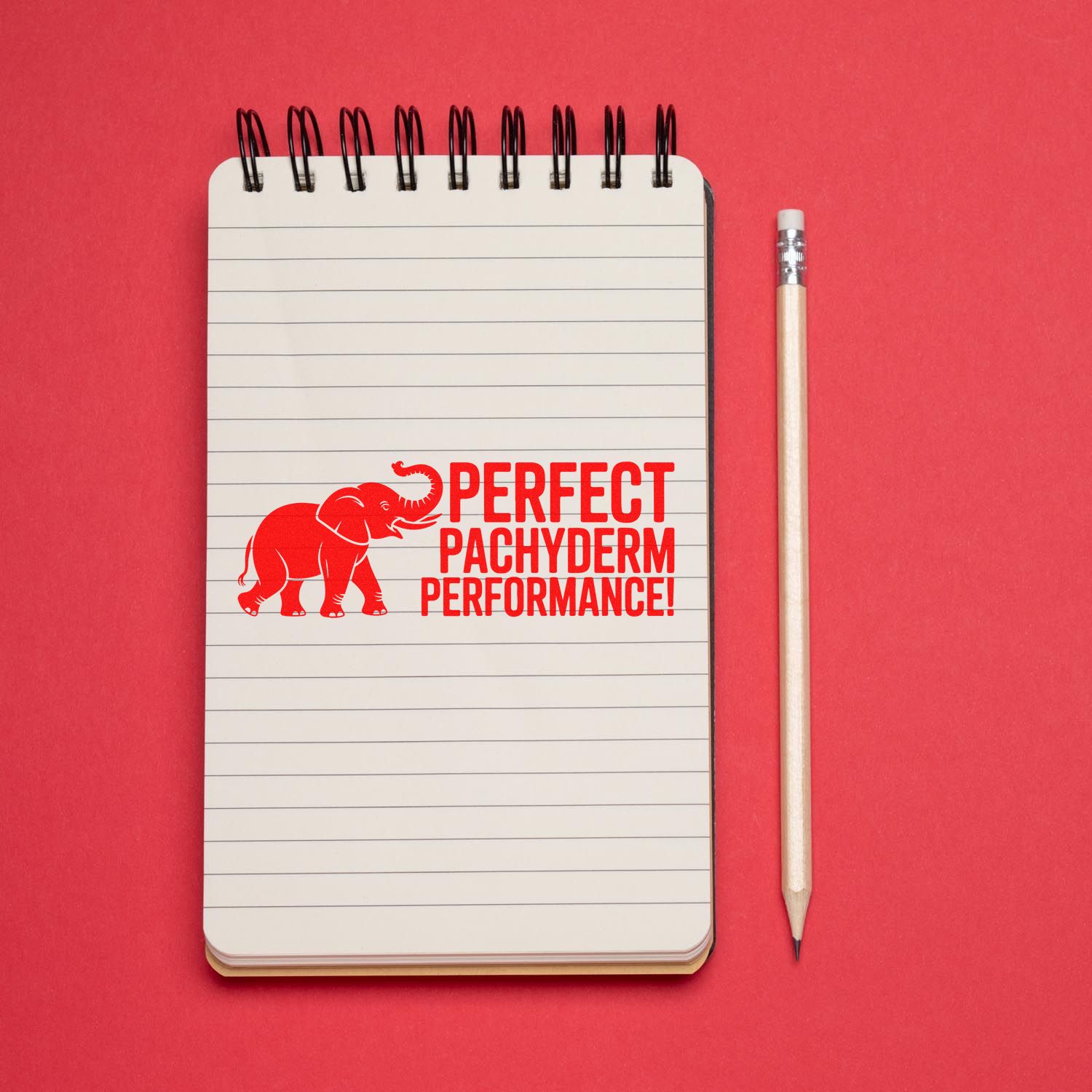 Red elephant rubber stamp/seal reading Perfect Pachyderm Performance on a lined notepad beside a pencil, on a red background.
