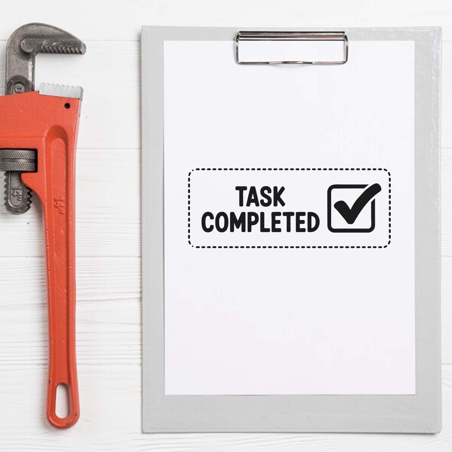 Red pipe wrench beside clipboard with black Task Completed stamp seal and checkmark on white paper.