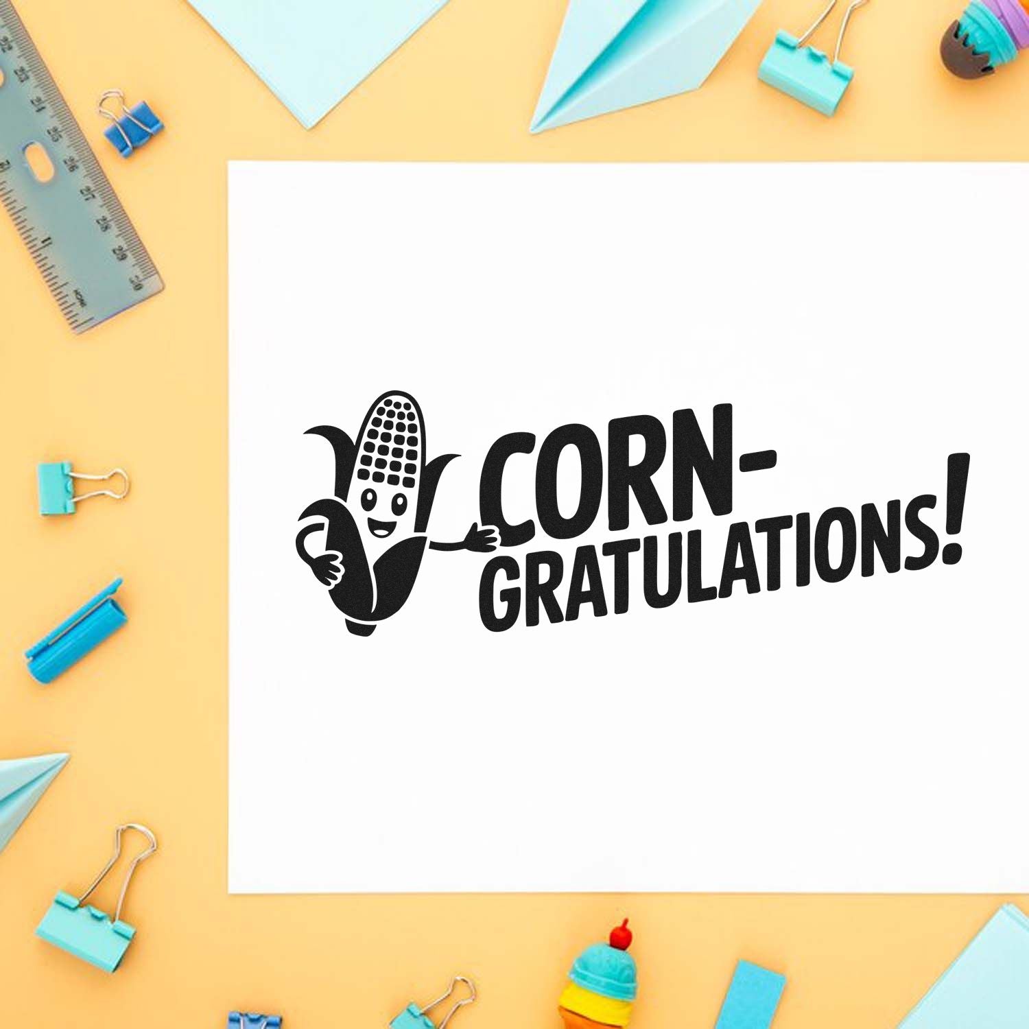 Black corn-gratulations stamp with smiling corn on white paper, surrounded by pastel blue clips, ruler, and paper planes.