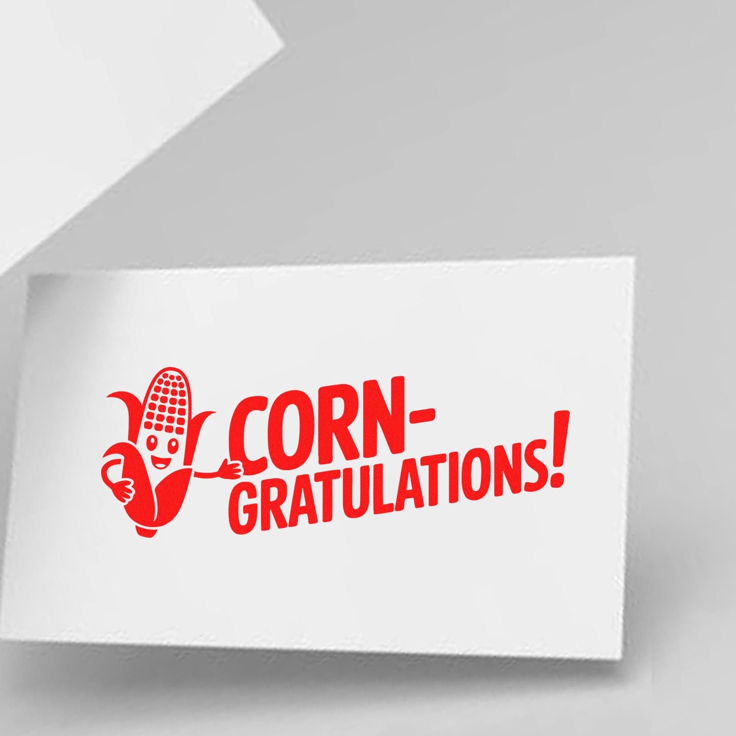 Red corn-themed rubber stamp seal on white card, with smiling corn mascot and bold CORN-GRATULATIONS! text.