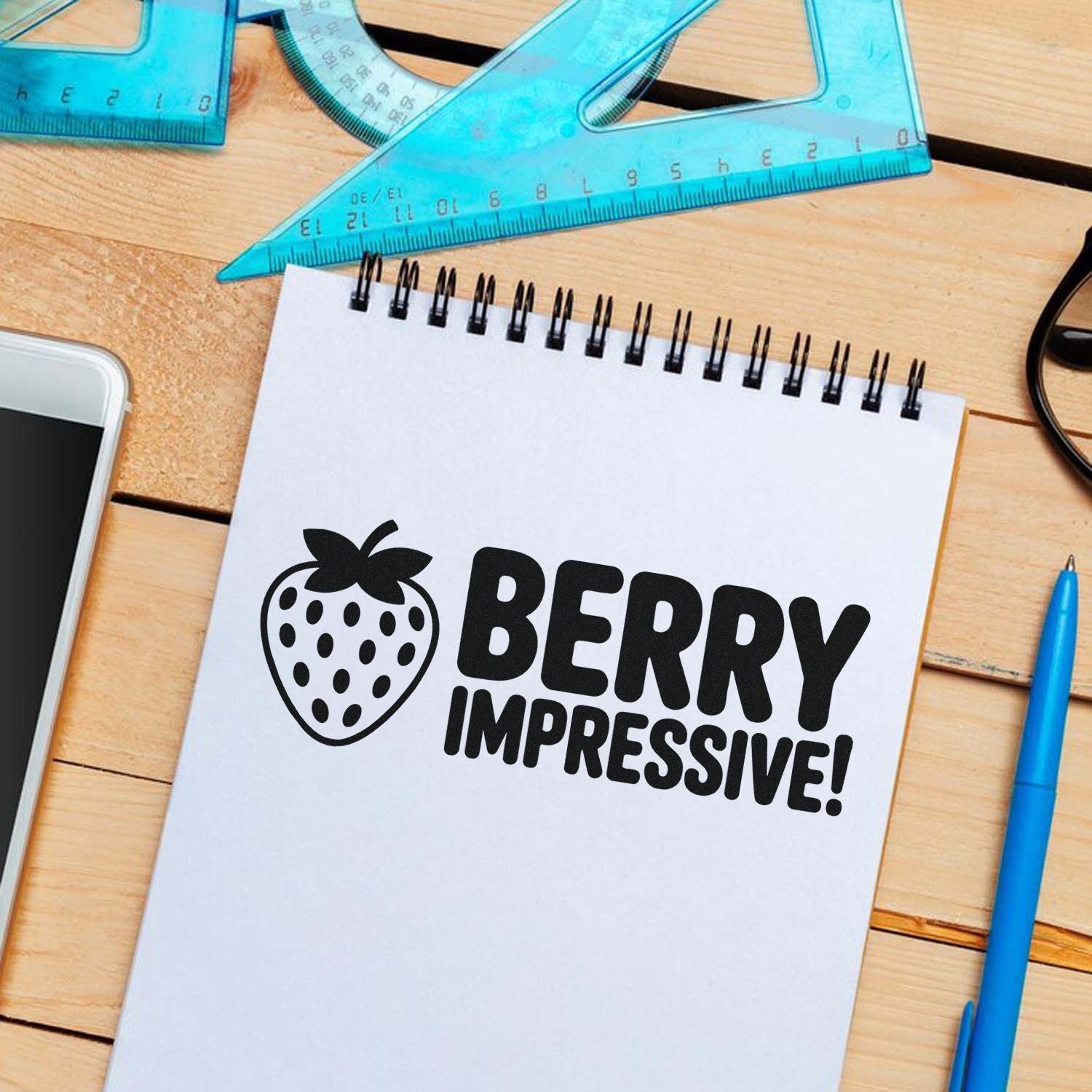 Black berry stamp seal design with strawberry icon on white notebook, with blue rulers and pen on a wooden desk.