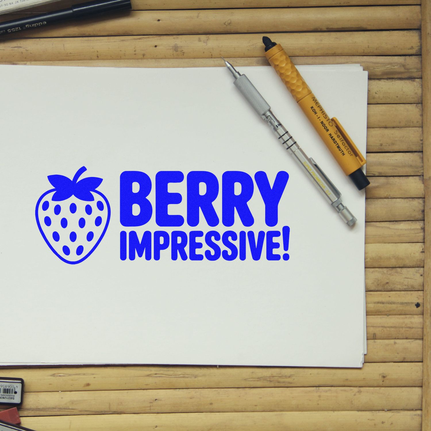 Blue strawberry stamp and seal with BERRY IMPRESSIVE! on white paper, beside orange and silver marking tools.
