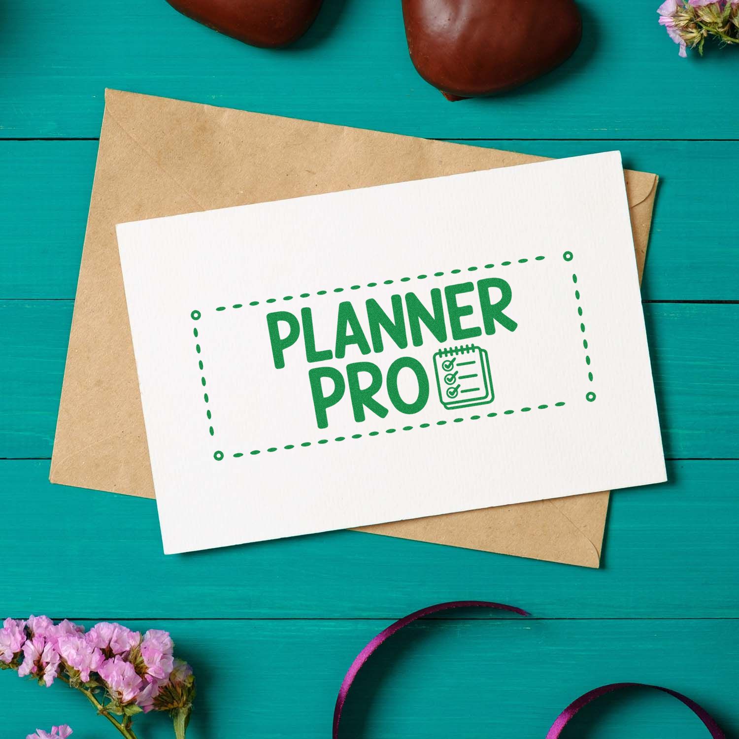 White card with green PLANNER PRO stamp seal on a brown envelope, set on a teal tabletop with flowers.