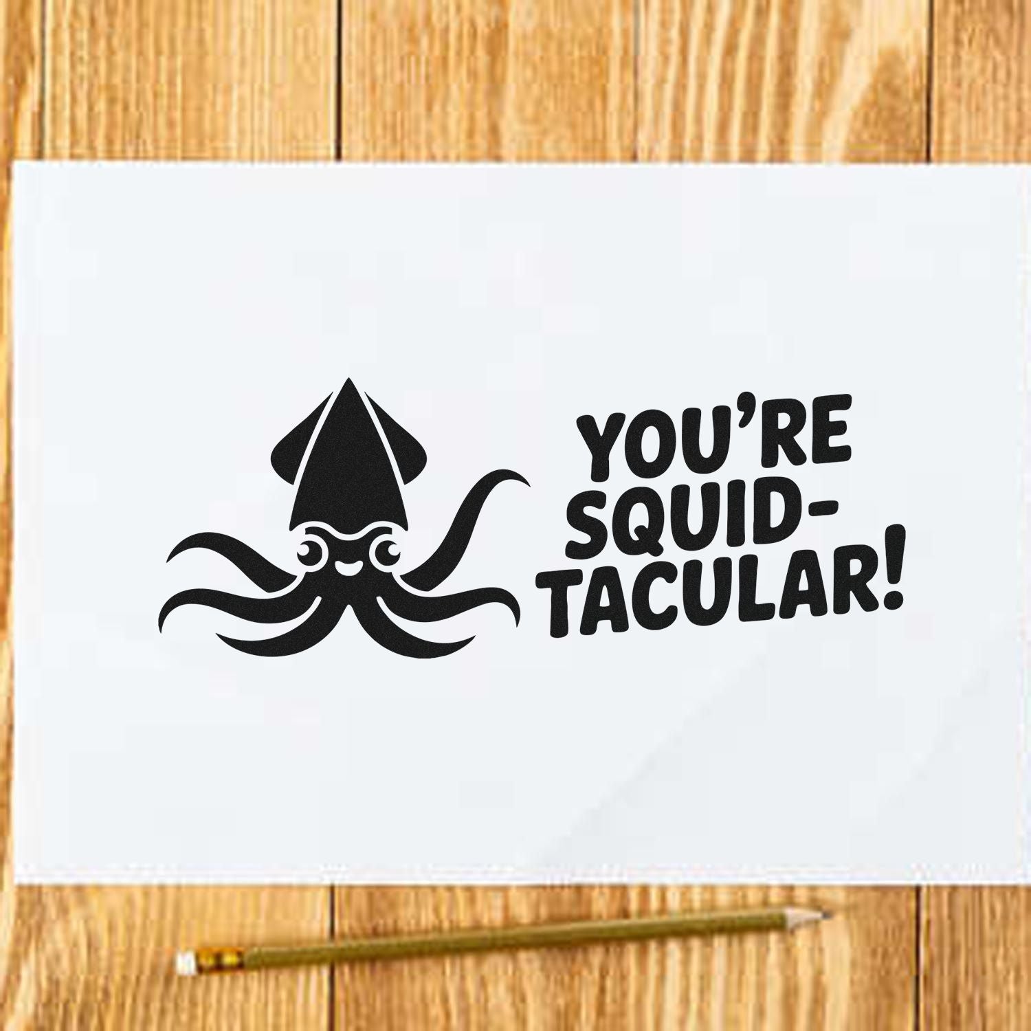 Black squid stamp and seal on white paper with YOURE SQUID-TACULAR! text on a wood background.