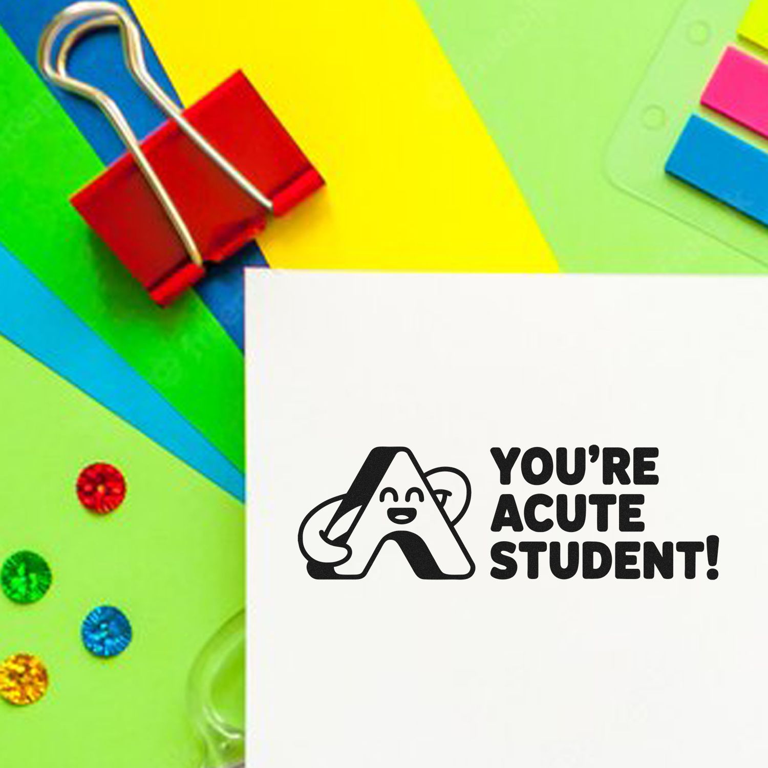 White rubber stamp reading Youre acute student! on bright neon paper with colorful clips, sticky notes and seal samples.