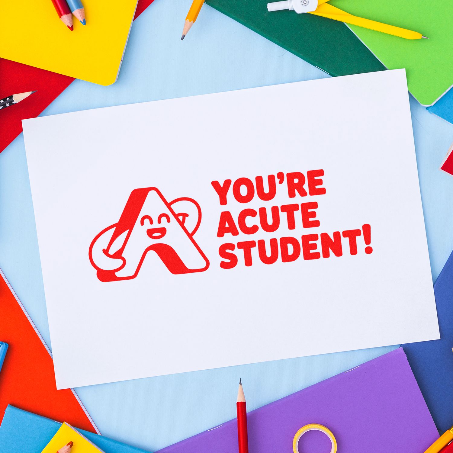 Red stamp seal reading Youre Acute Student! on white paper, with colorful notebooks and pencils around.