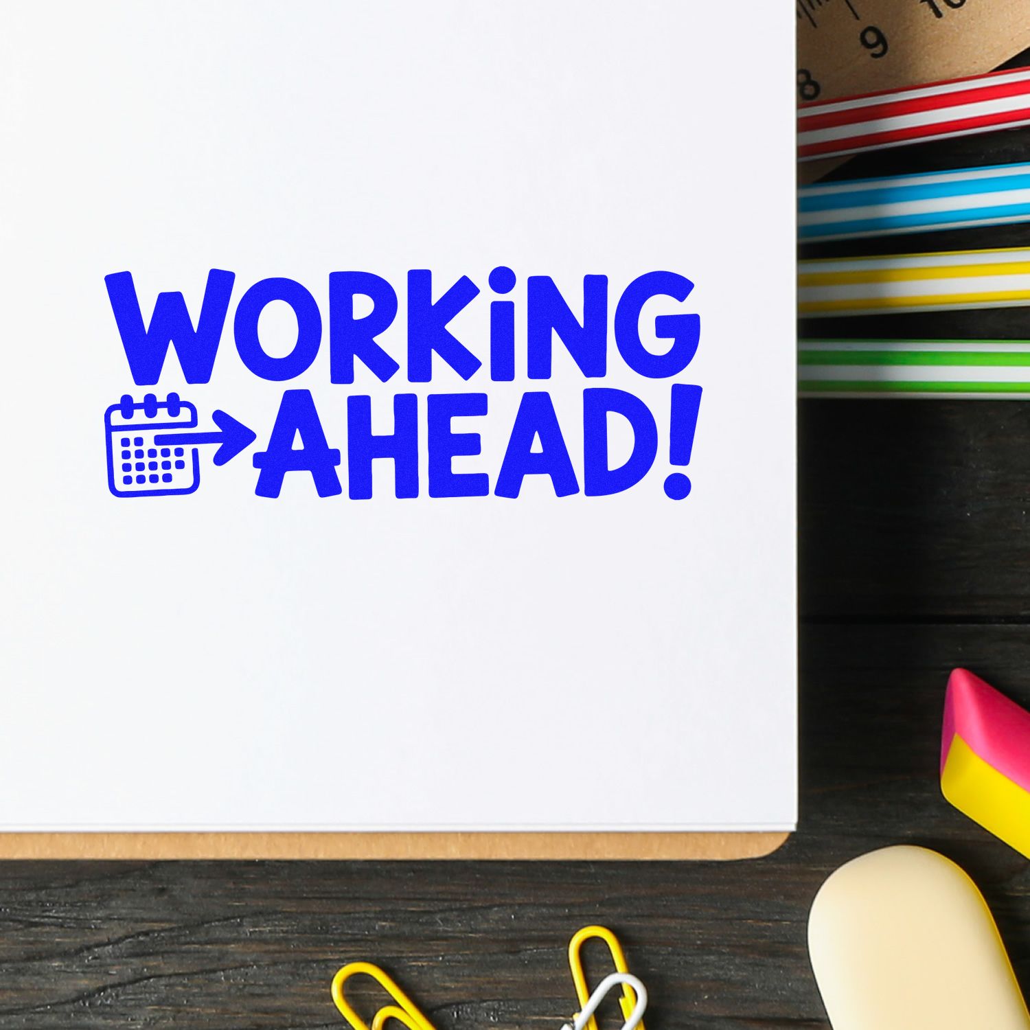 Blue WORKING AHEAD! stamp with calendar icon on white paper, beside colorful seal and stamp products.