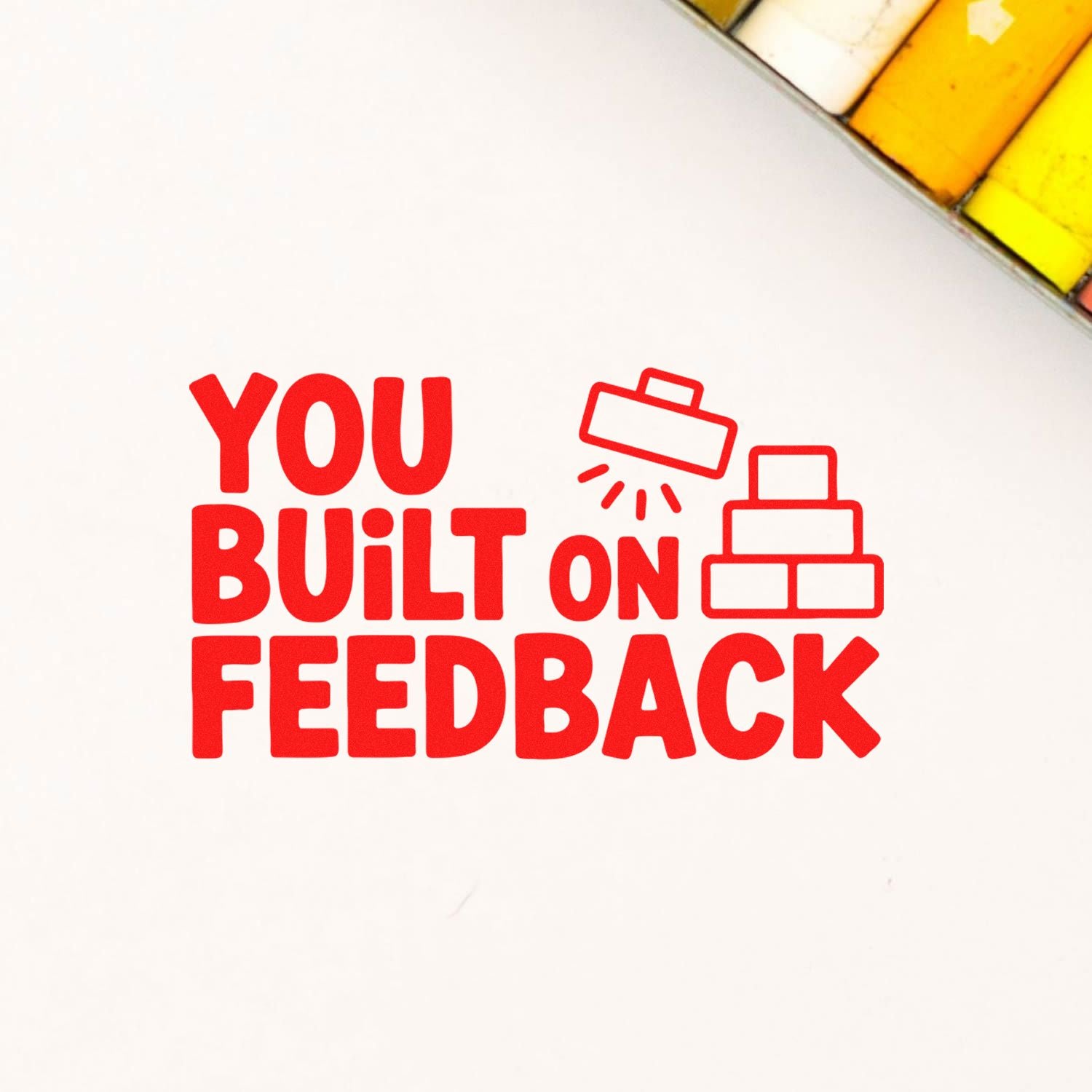 Red stamp and seal design reading YOU BUILT ON FEEDBACK, with a stamp icon, stacked blocks, on a white background with yellow corner accents.