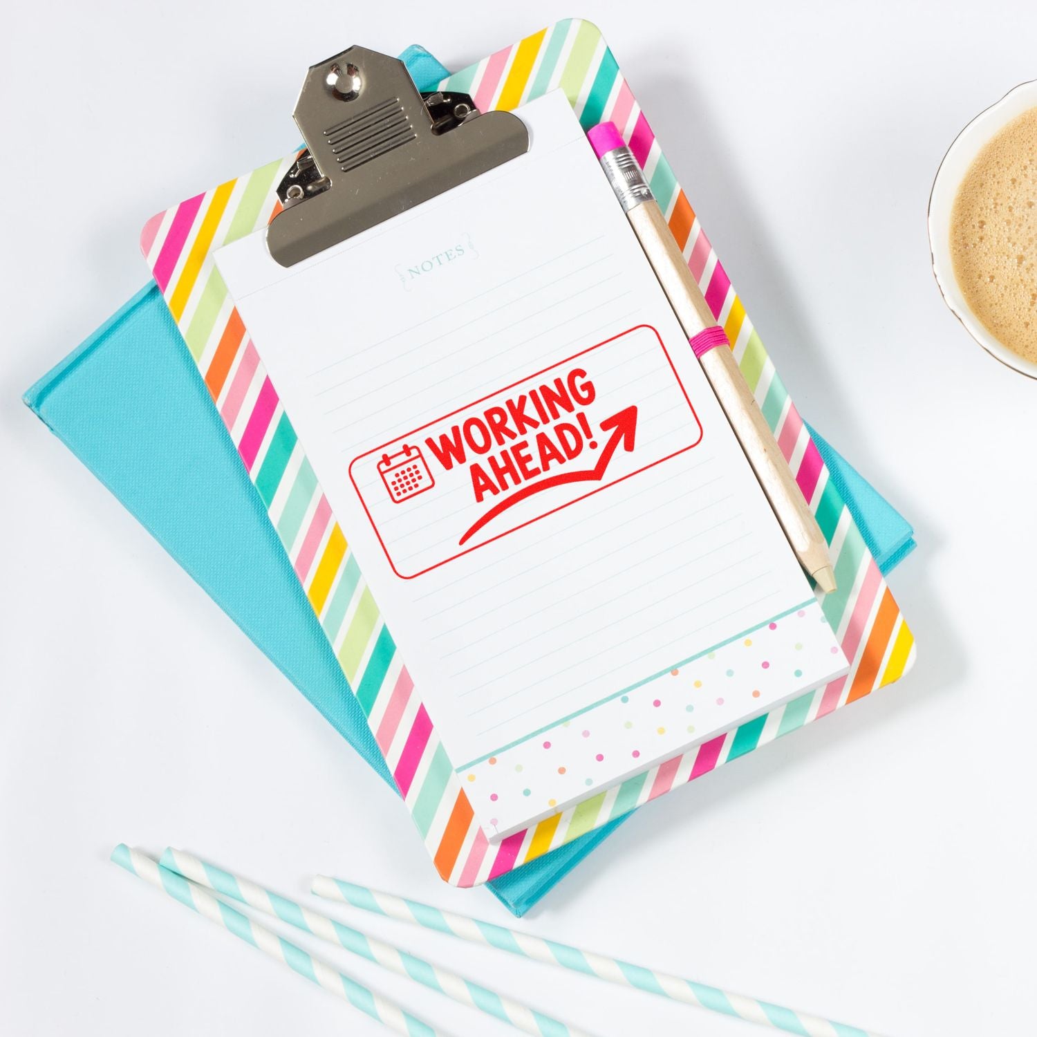 Colorful clipboard notepad with red Working Ahead! stamp, striped cover, pencil, and seal-ready desk accessories.