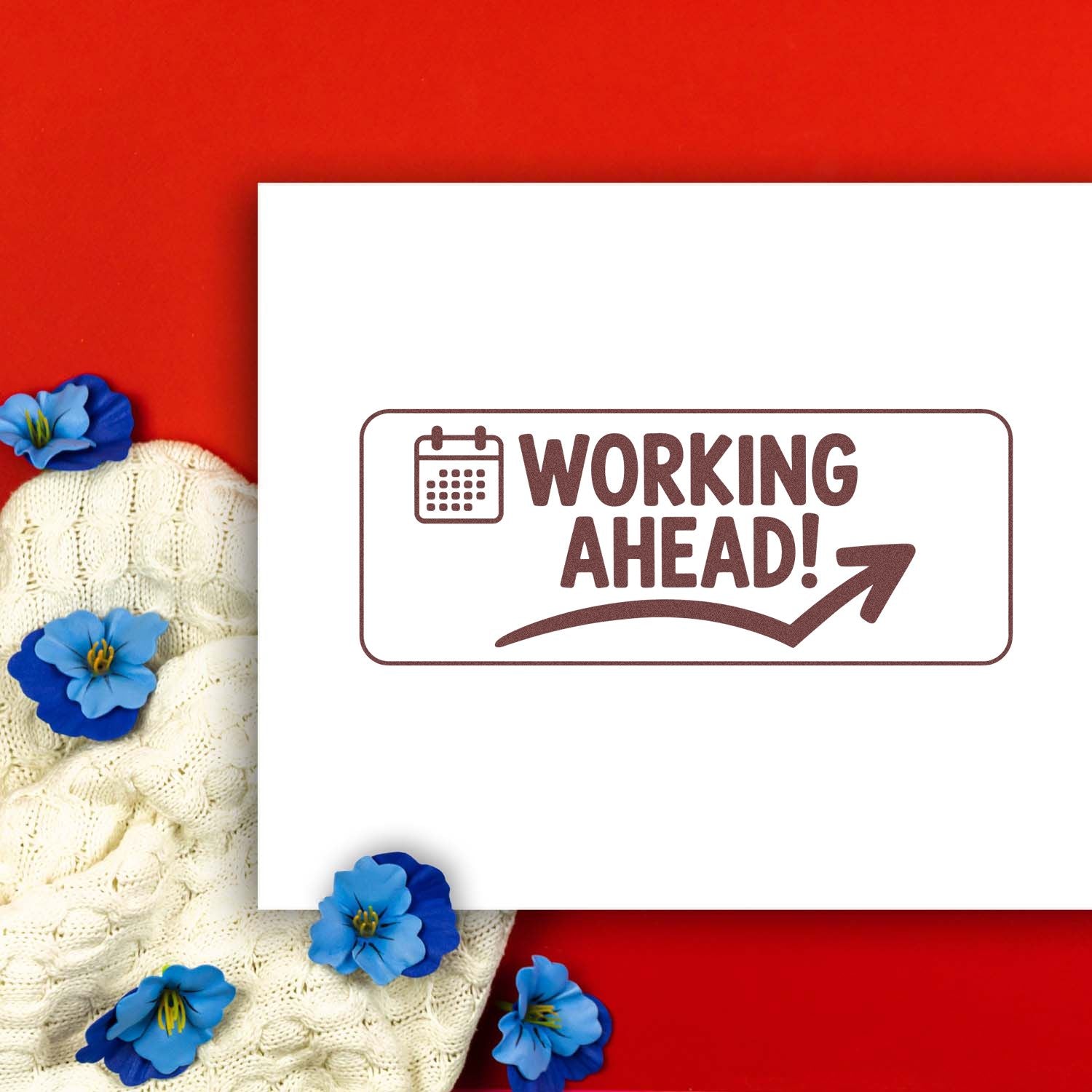 Brown Working Ahead! rubber stamp with calendar icon on white card, on red background with cream knit and blue flowers.