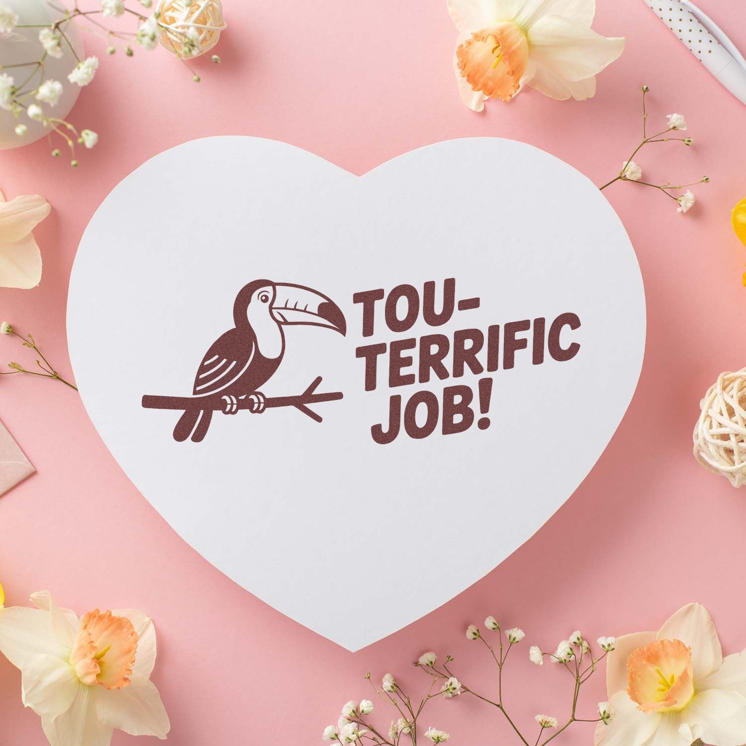 Heart-shaped white stamp seal with maroon toucan and TOU-TERRIFIC JOB! on a pink floral background