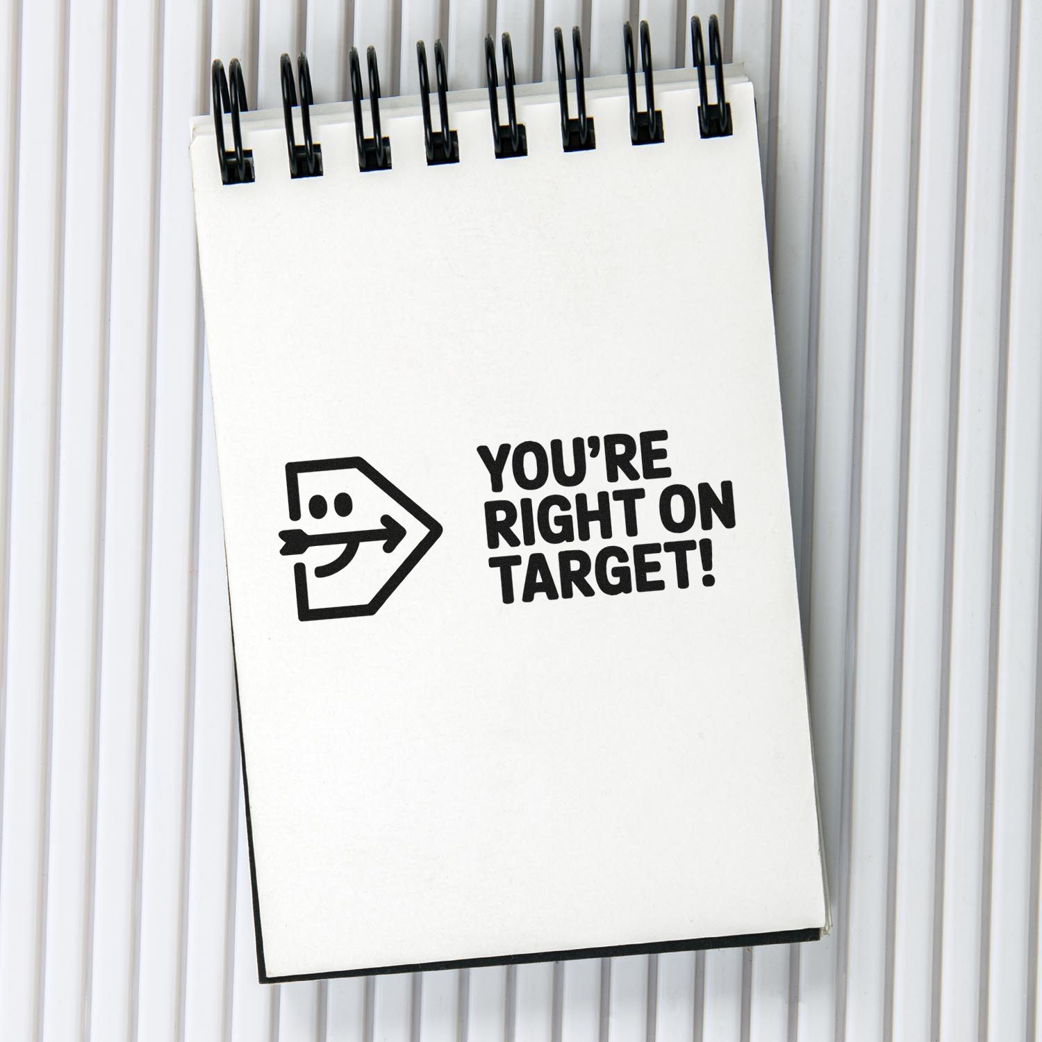 Black self-inking stamp and seal design on a white spiral notepad, reading Youre right on target! with arrow logo.