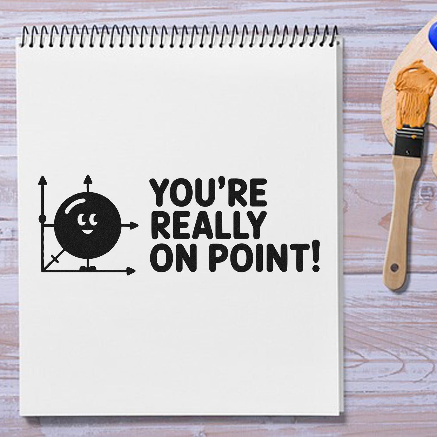 Black motivational stamp on a white spiral notebook, with a wooden stamp tool beside it and bold text saying YOURE REALLY ON POINT!