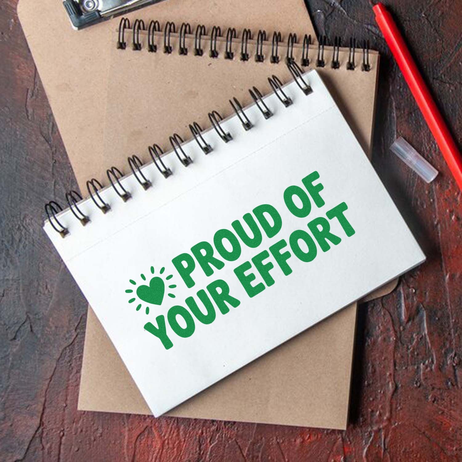 Green Proud of Your Effort stamp and seal on a white spiral notebook with heart icon, set on kraft paper.